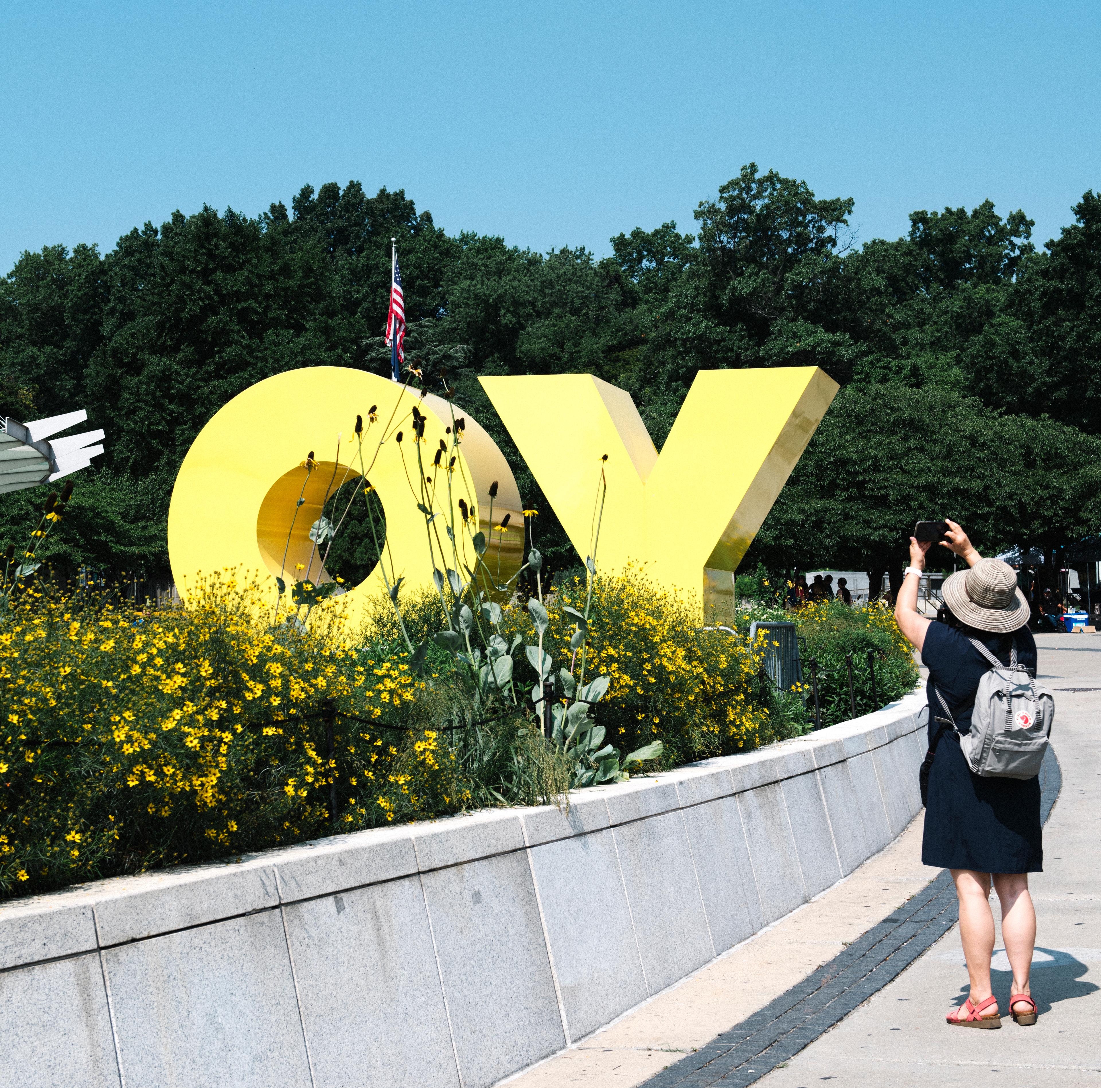 A person taking a picture of an artwork reading “OY”