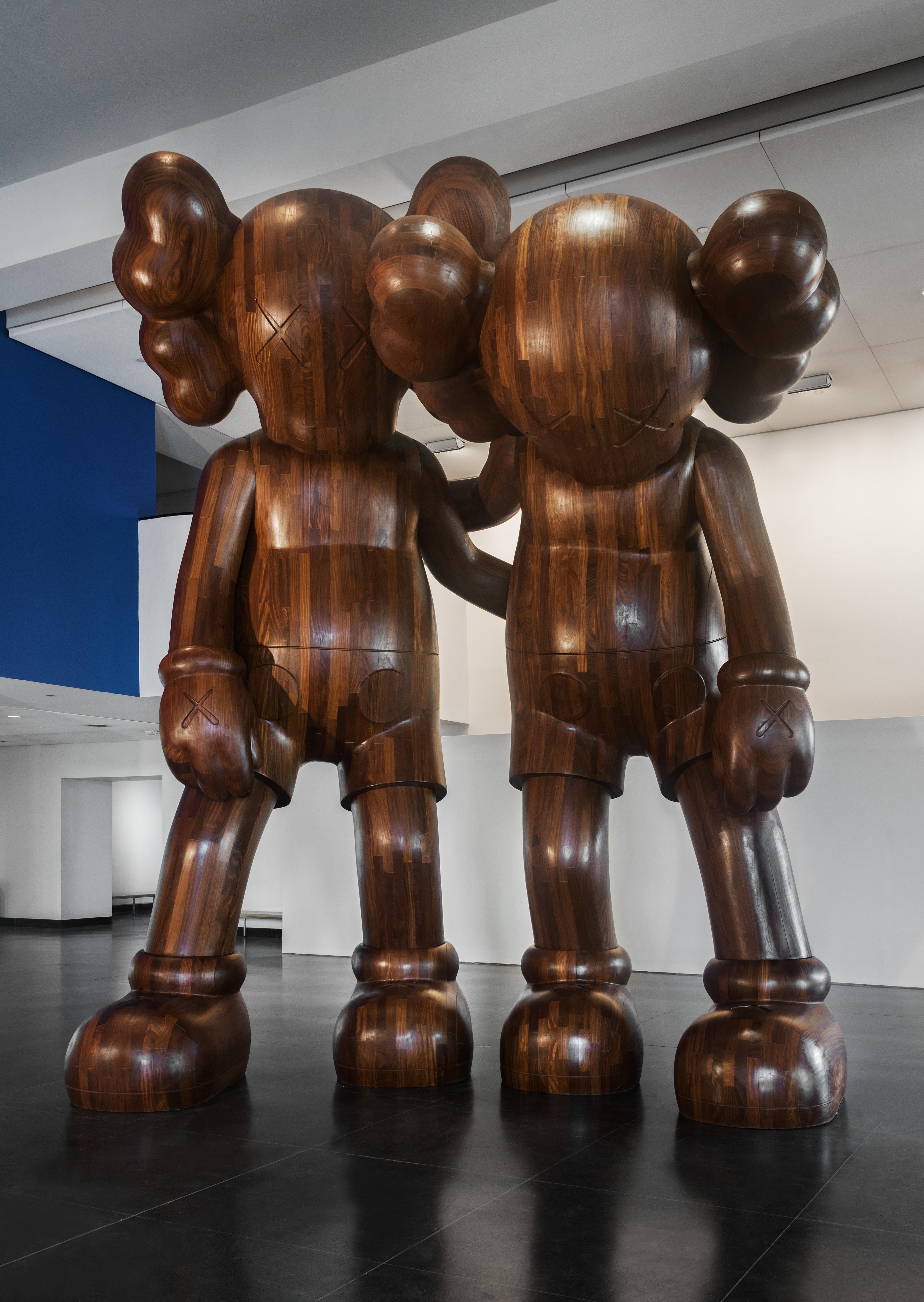 A wooden sculpture of two colossal cartoon figures leaning on one another