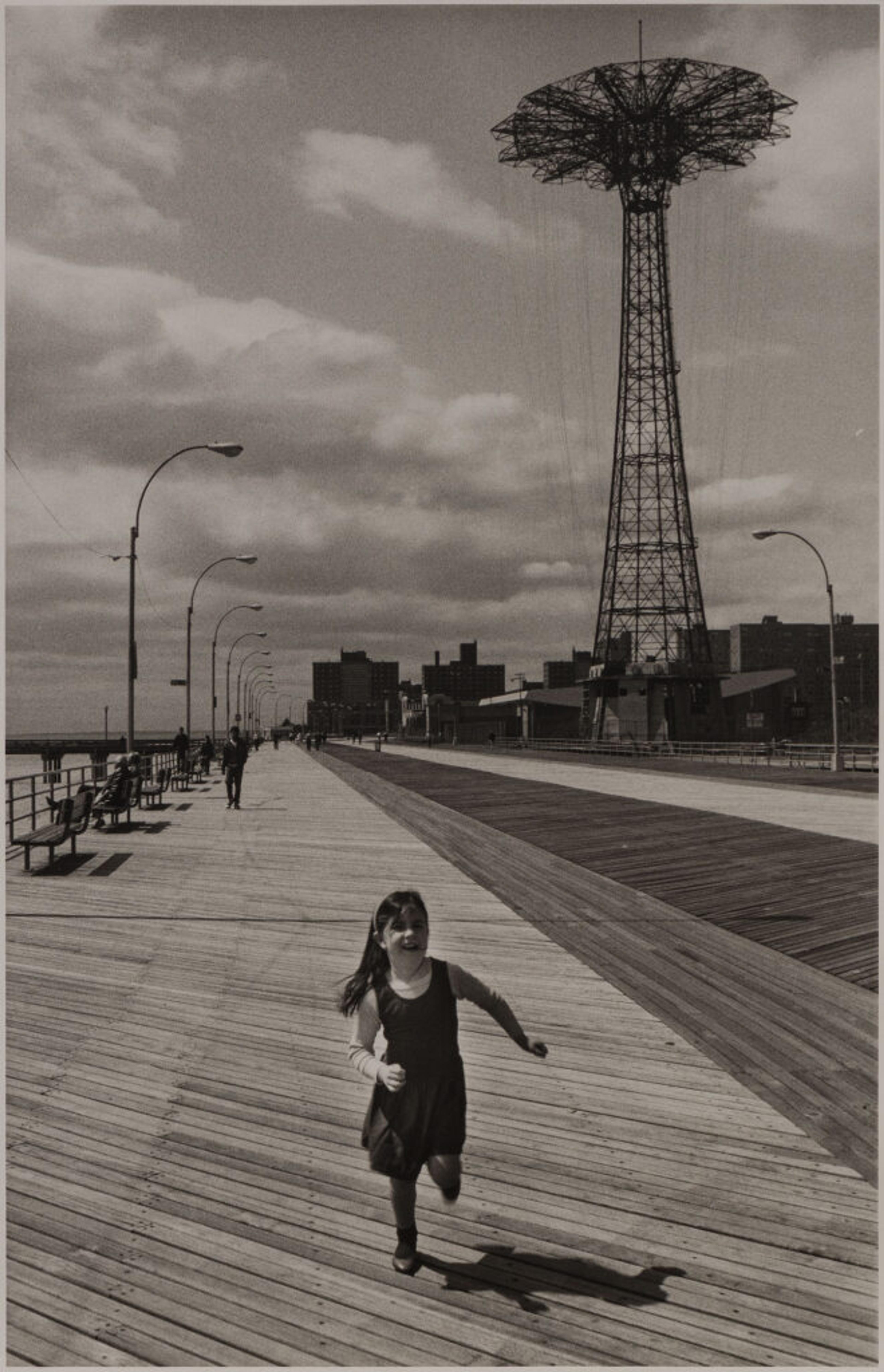 Girl running along Coney Island boardwalk beneath Parachute Jump tower