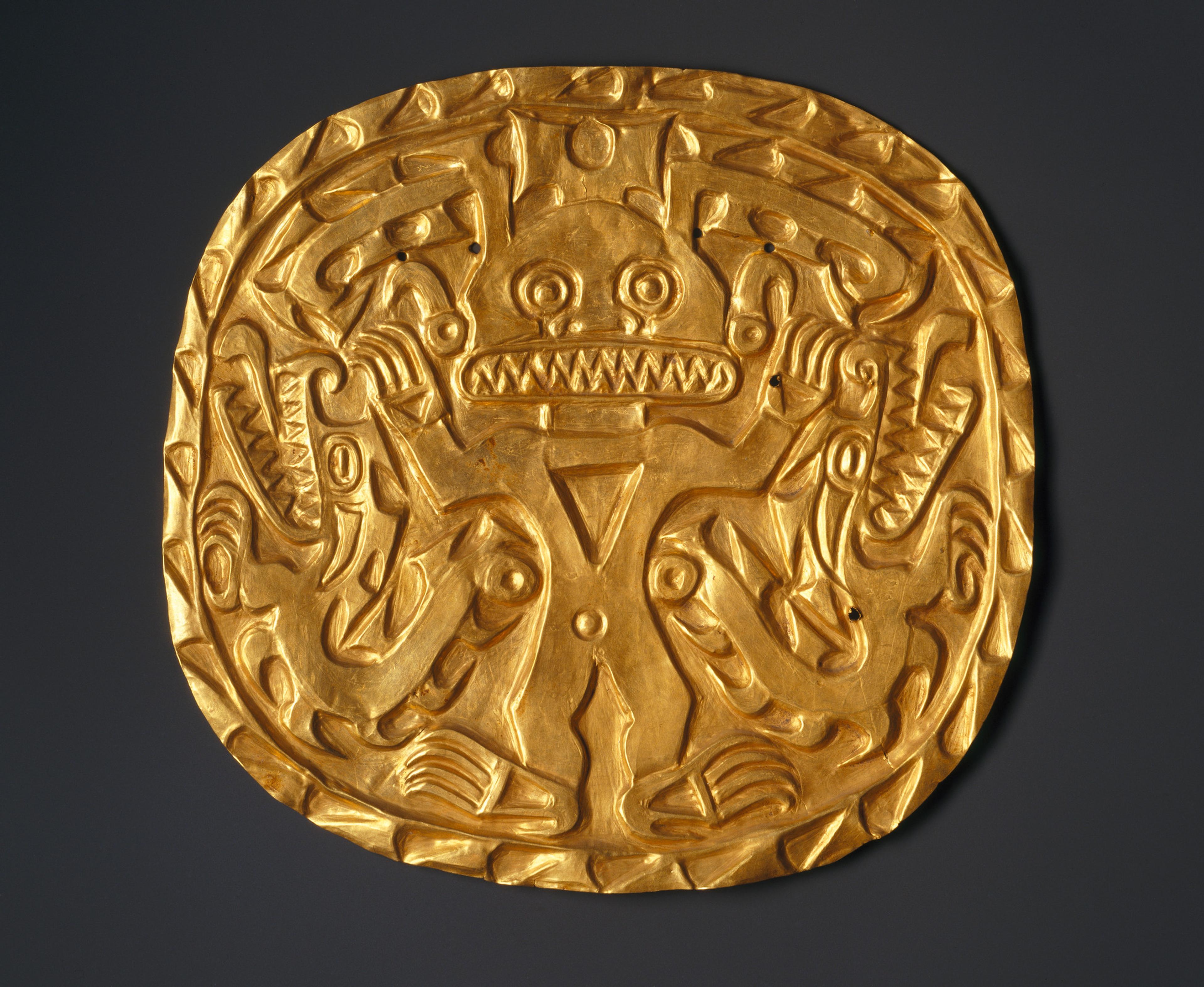 A circular gold object that features animal figure with large teeth centered on a black bacground