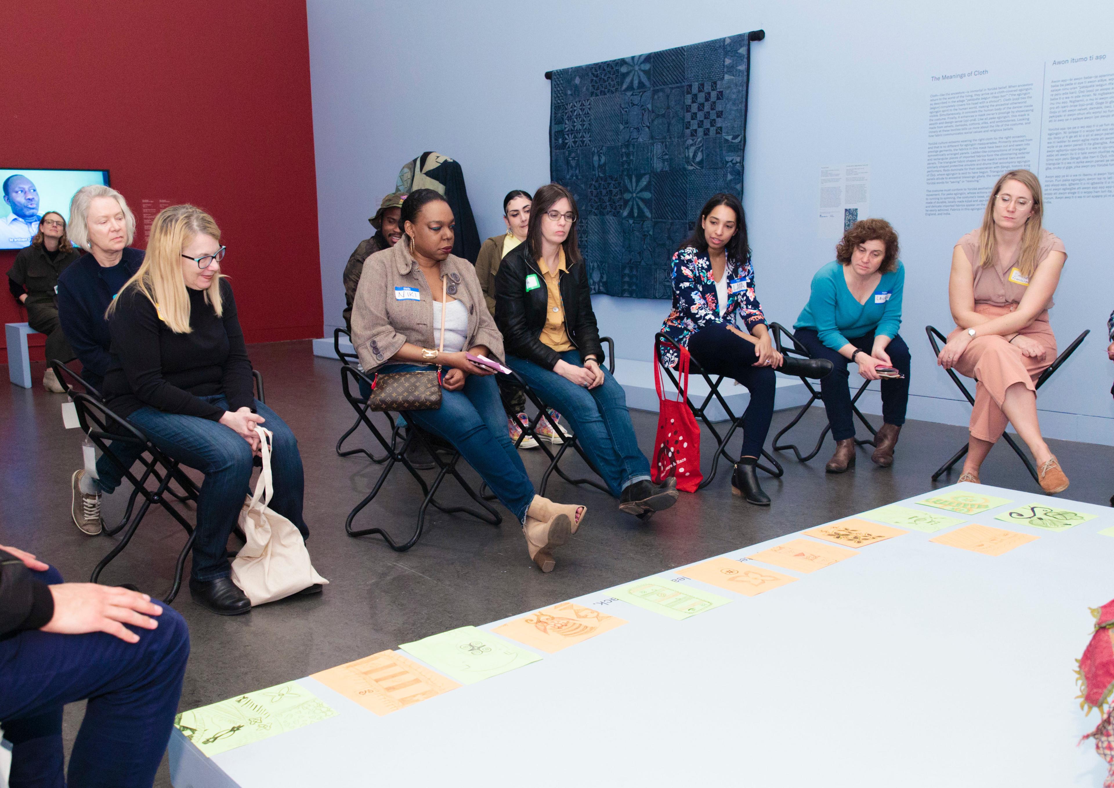 A group of adults look down at a row of drawing that have been laid out in an art gallery