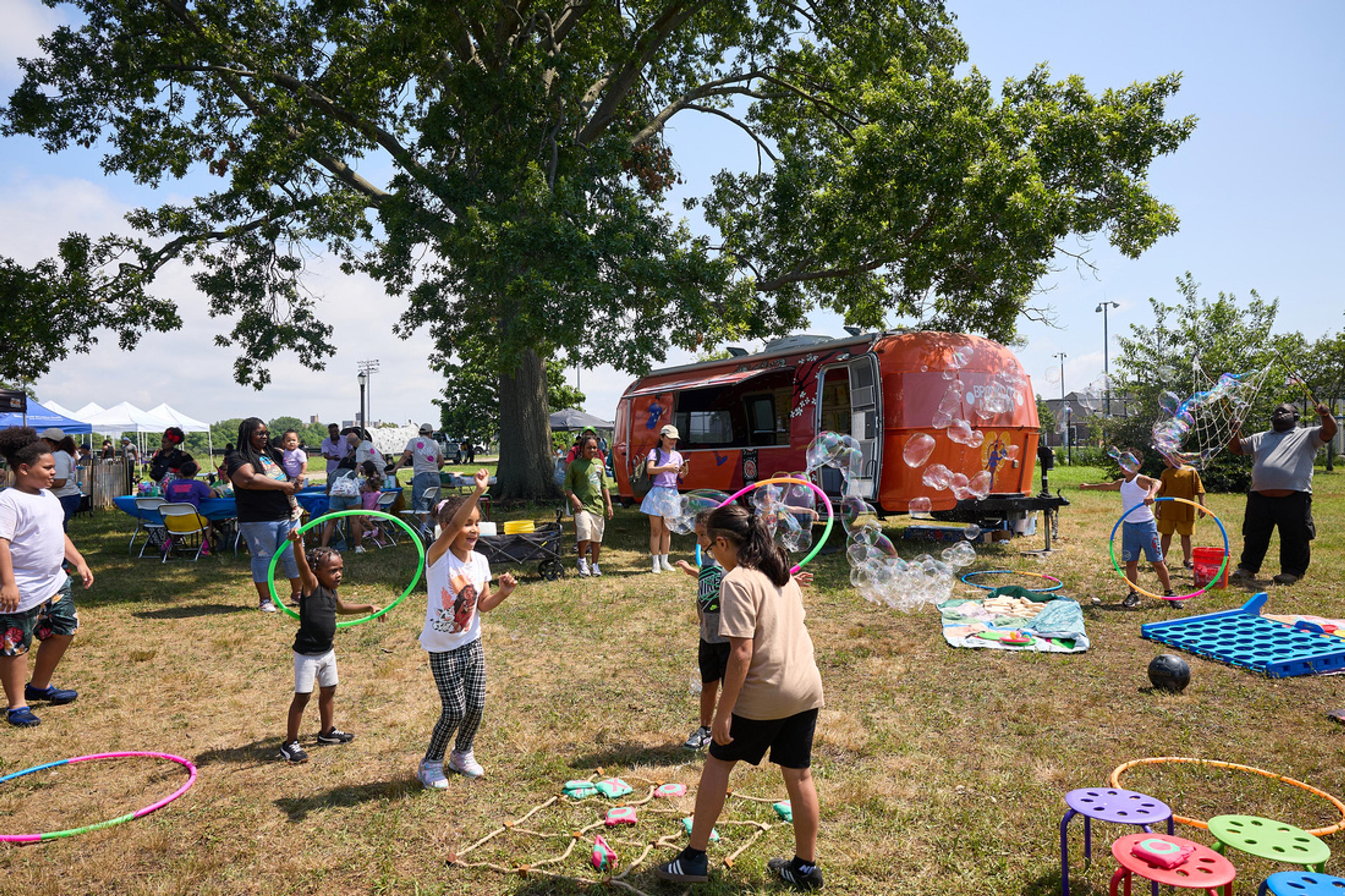 Children hula-hooping and people blowing bubbles outside near an Airstream trailer
