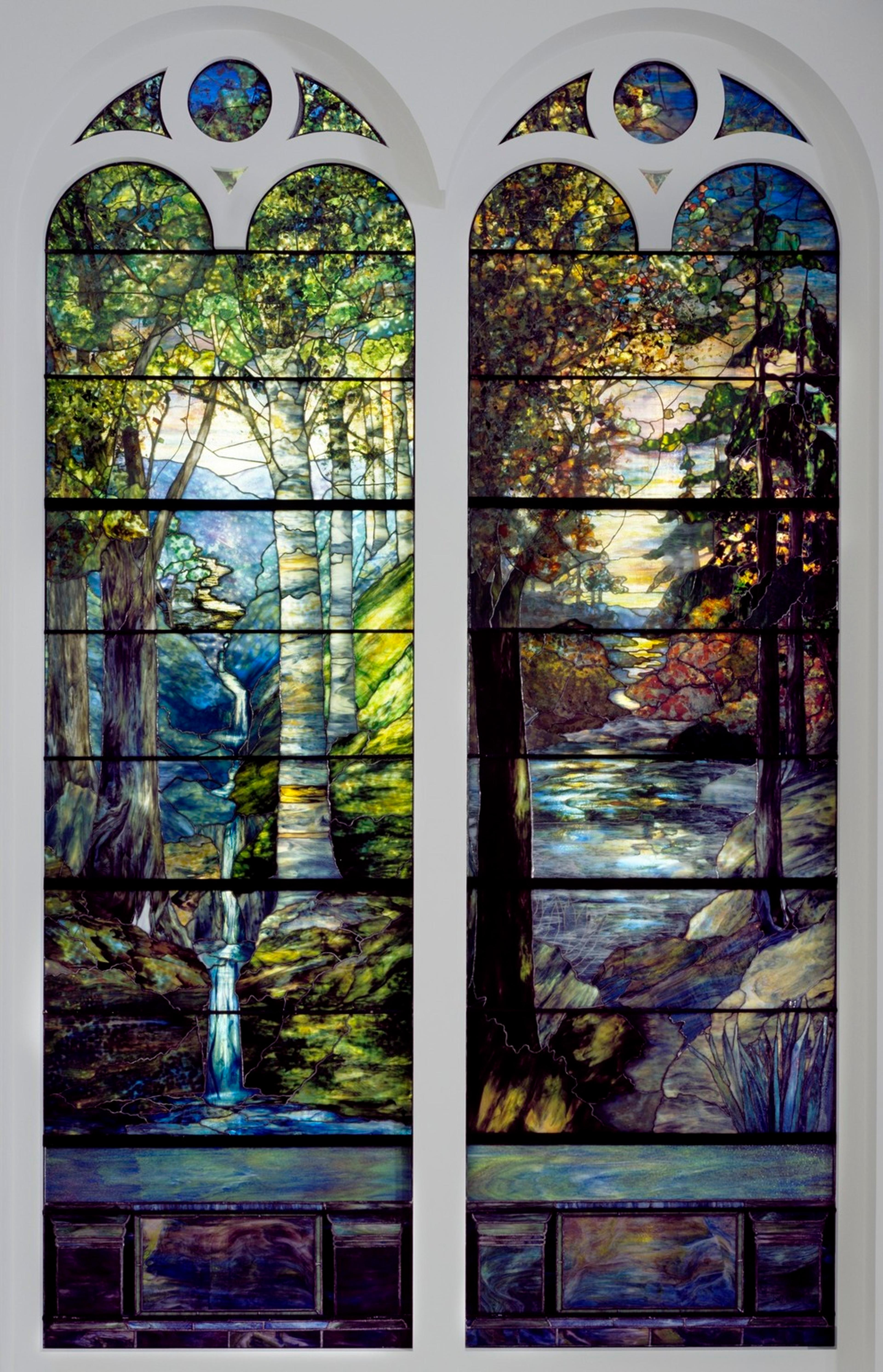 Two detailed image made from colored glass depict spring and autumn in a wooded area with a stream