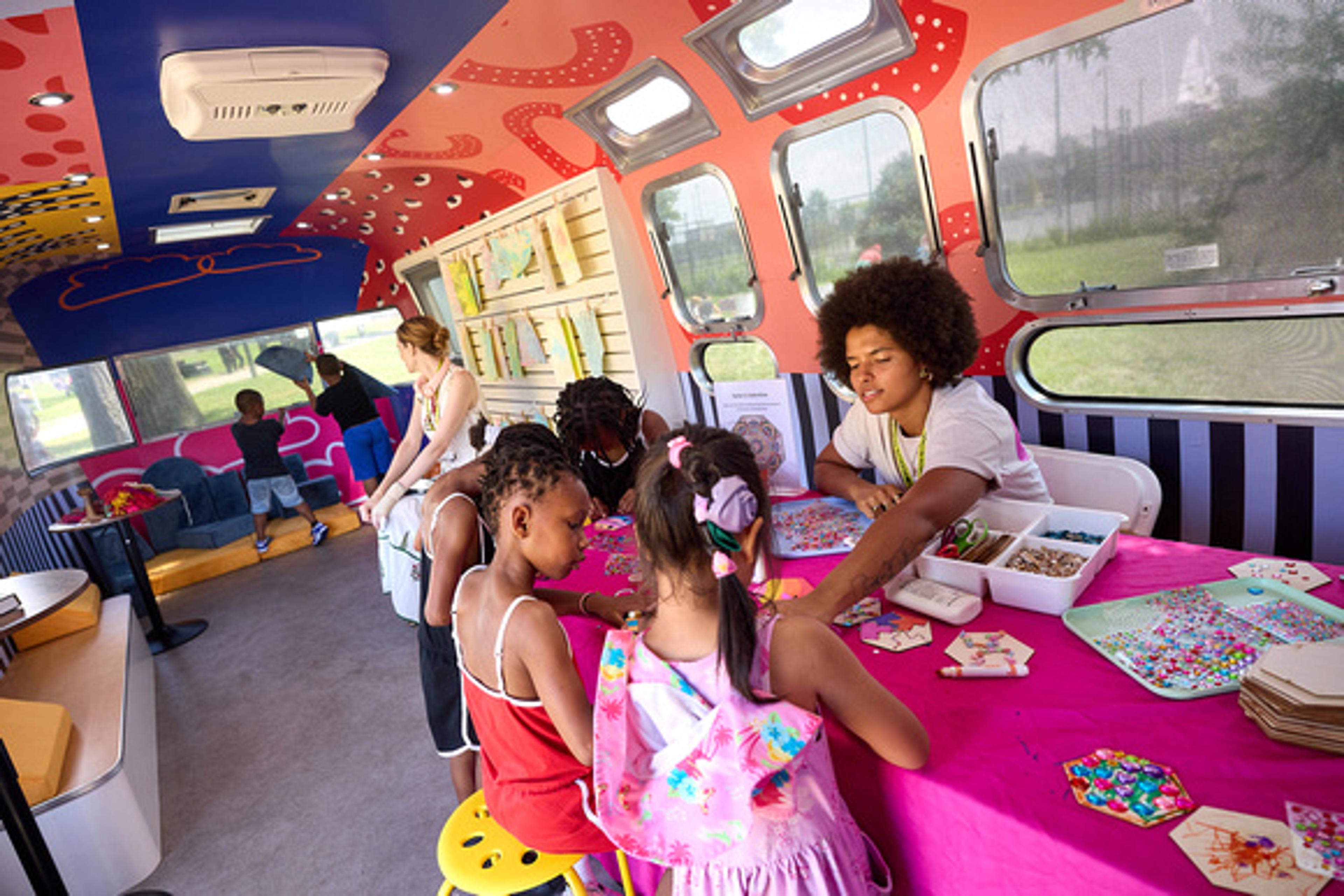 Children making art at a table inside a colorful trailer