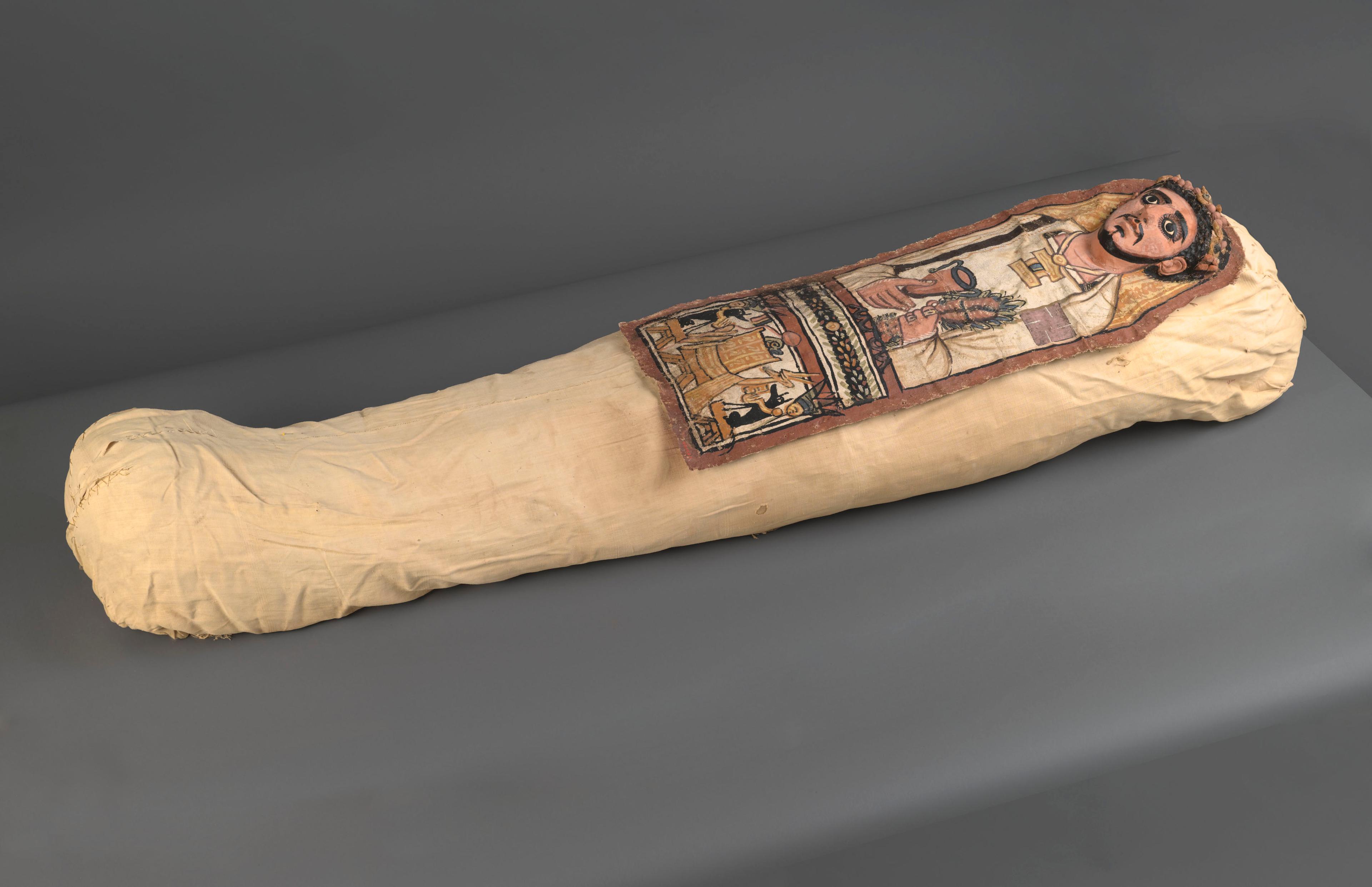 Cartonnage and Mummy of an Anonymous Man. Egypt, excavated in Deir el Bahri. Roman Period, 3rd century C.E. Linen, plaster, paint, organic materials; cartonnage: 131⁄4 × 357⁄16 in. (33.7 × 90 cm); mummy, approximately: 8 × 20 × 62 in. (20.3 × 50.8 × 157.5 cm). Brooklyn Museum, Charles Edwin Wilbour Fund, 52.128a–e