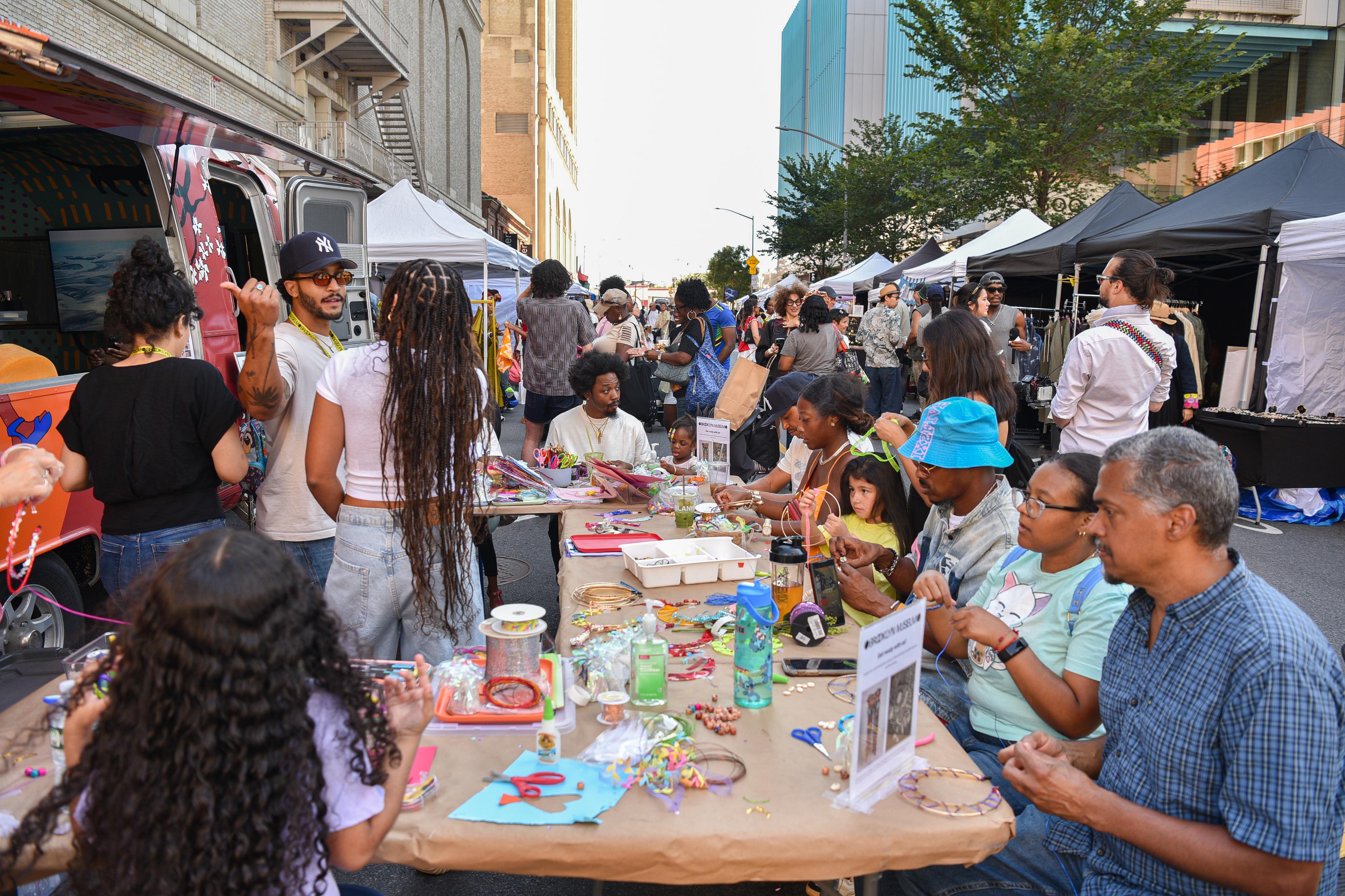 People making beaded jewelry at a table amid a street fair