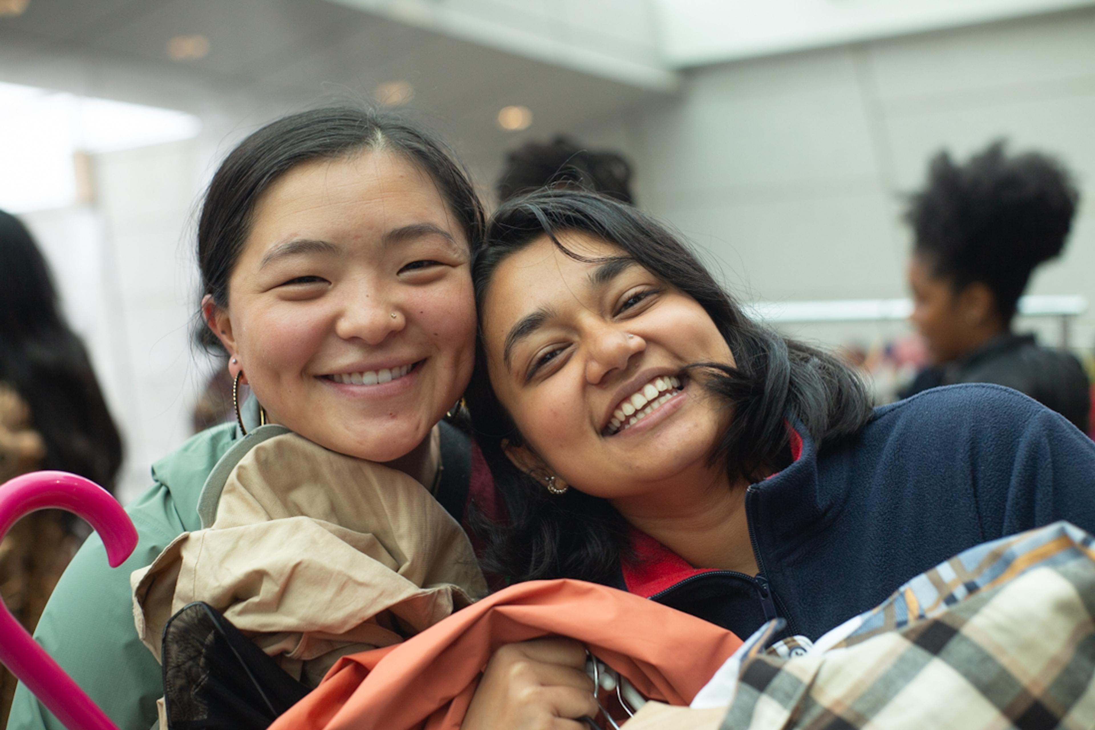 A pair of adults smiling close to one another hold a armful of clothing