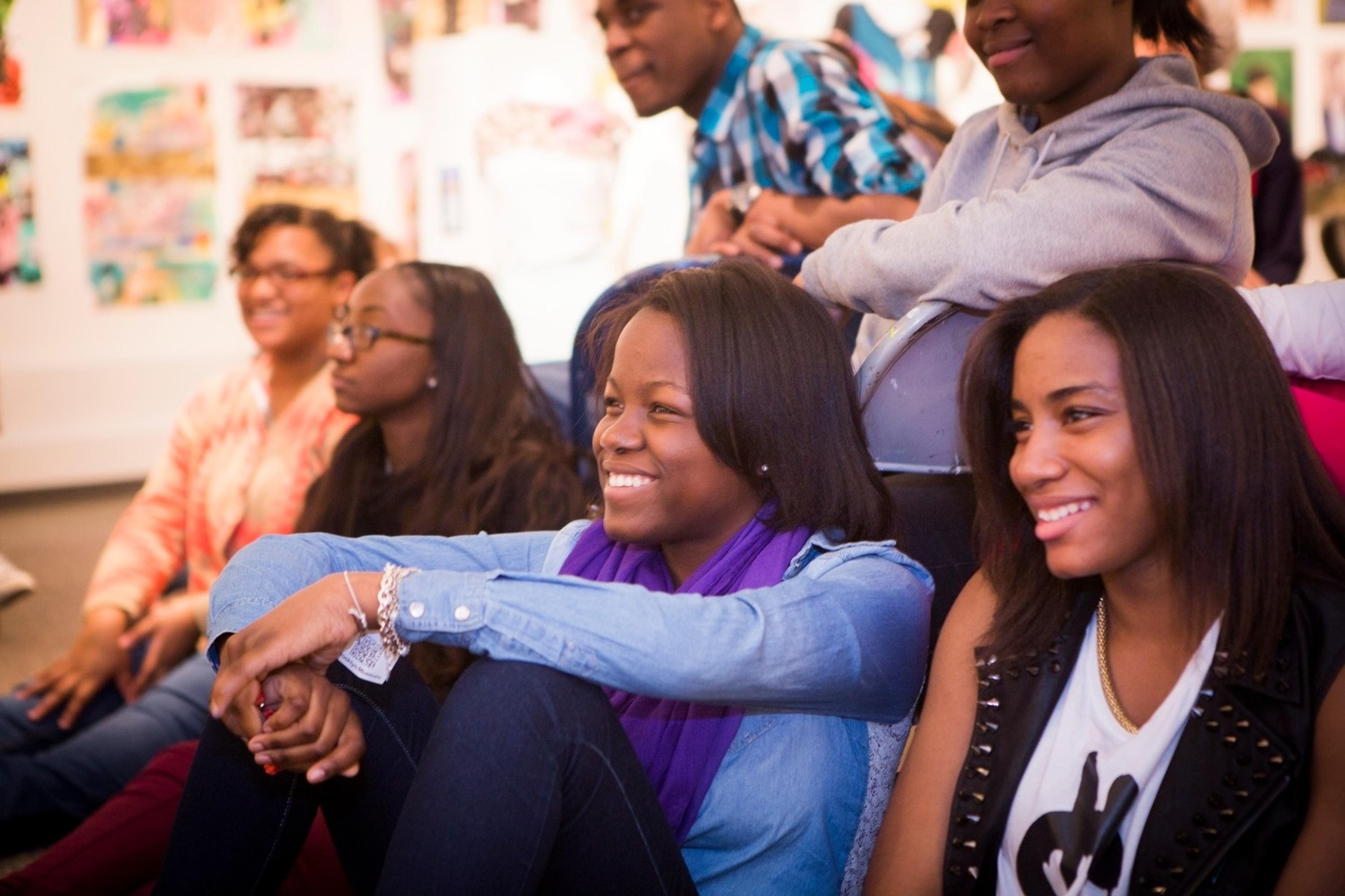 A group of seated students all look toward something out of frame