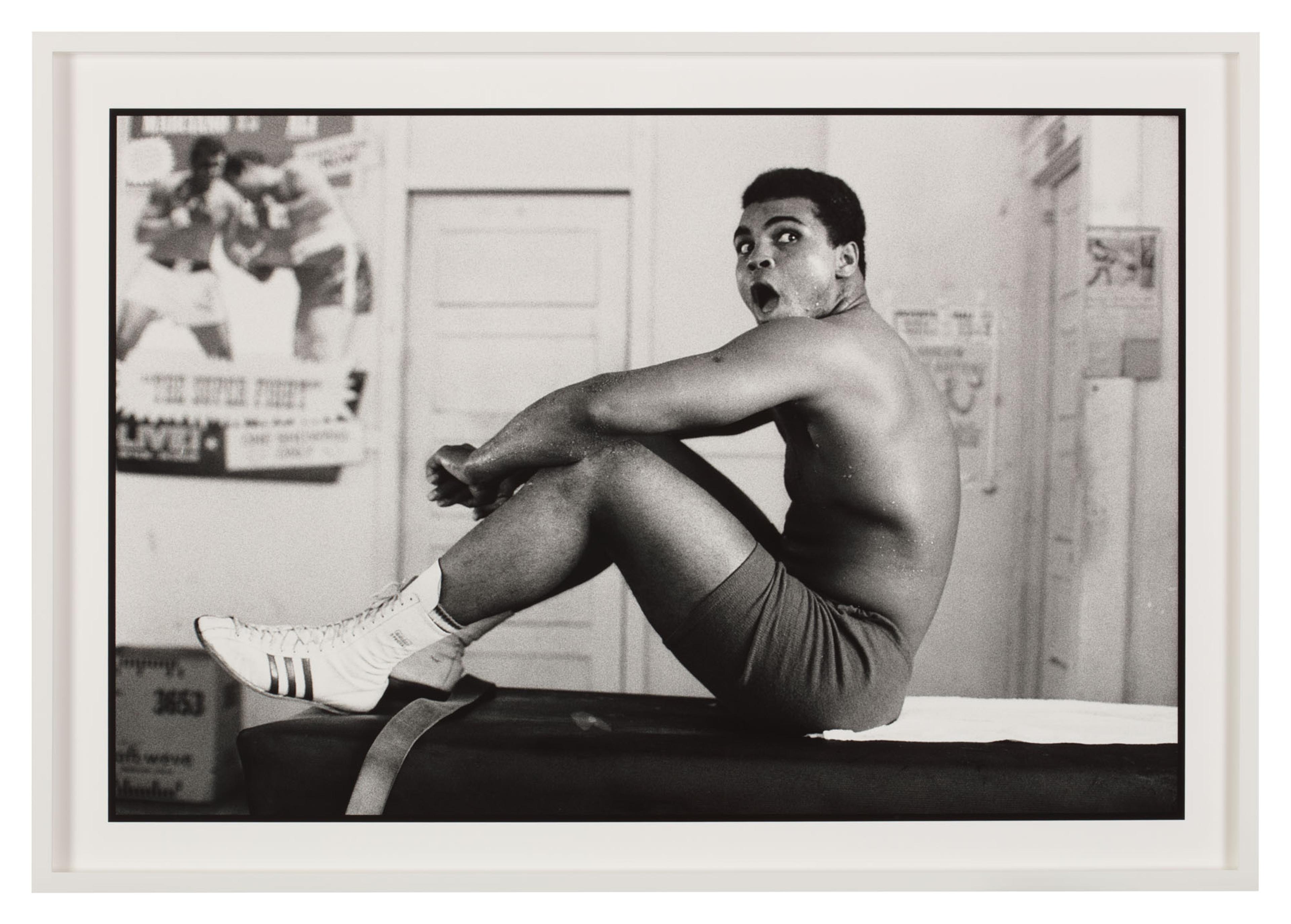 Black-and-white photograph of Muhammad Ali sitting on a table