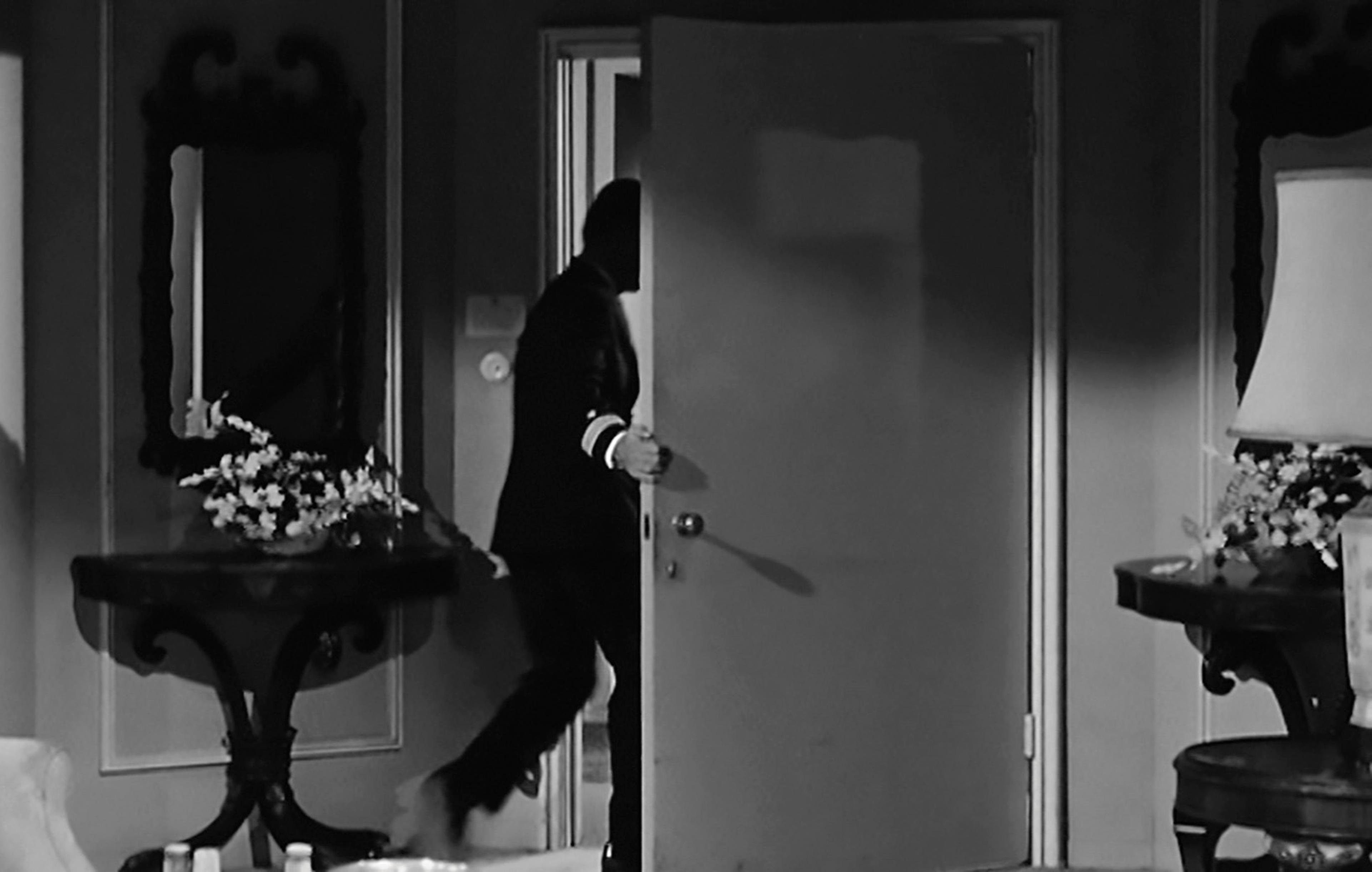 Black-and-white still showing a man walking through a doorway
