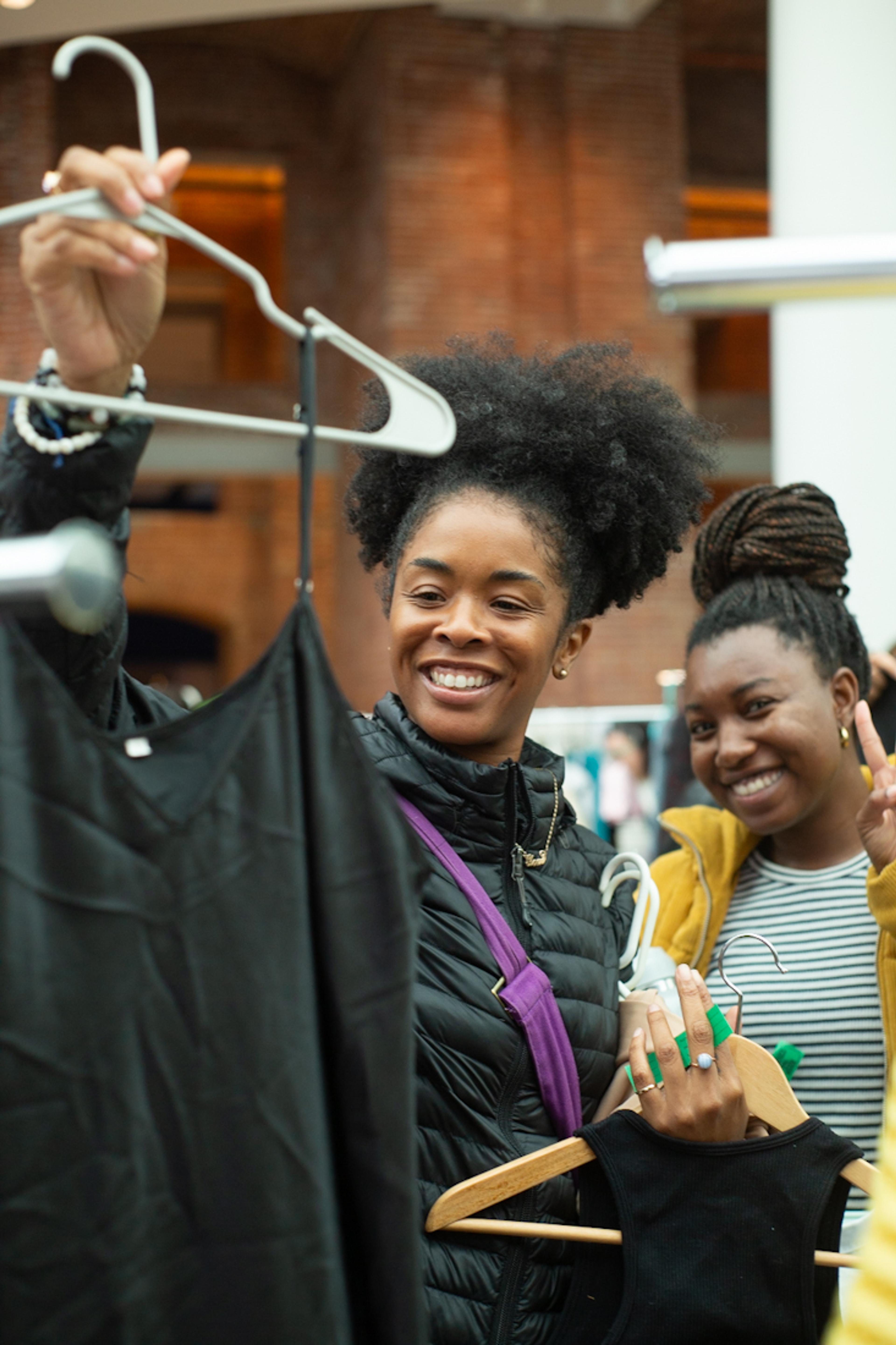 Two adults smile and hold two black dresses on hangers