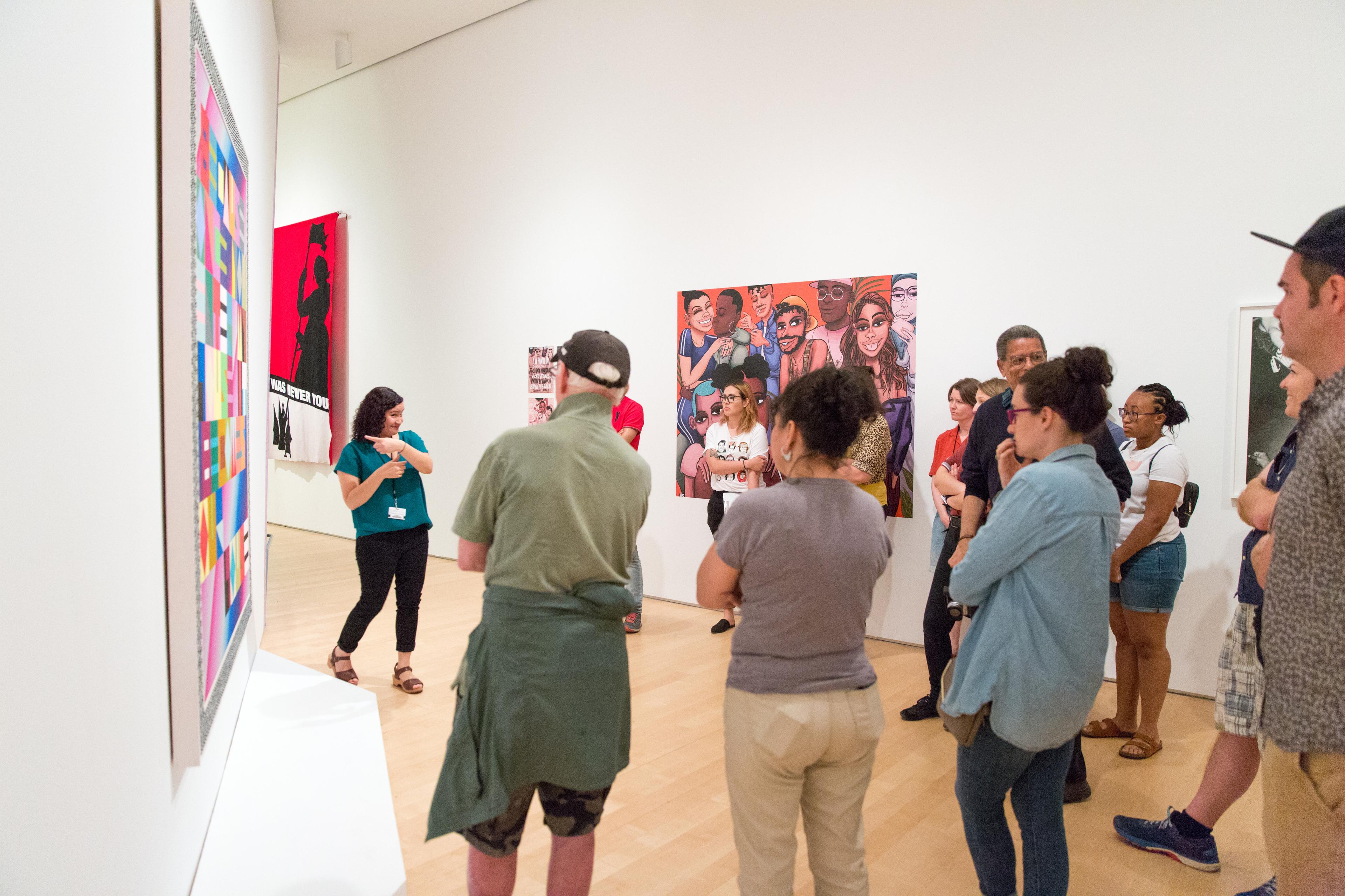 A tour group watches a guide sign in front of a large painting