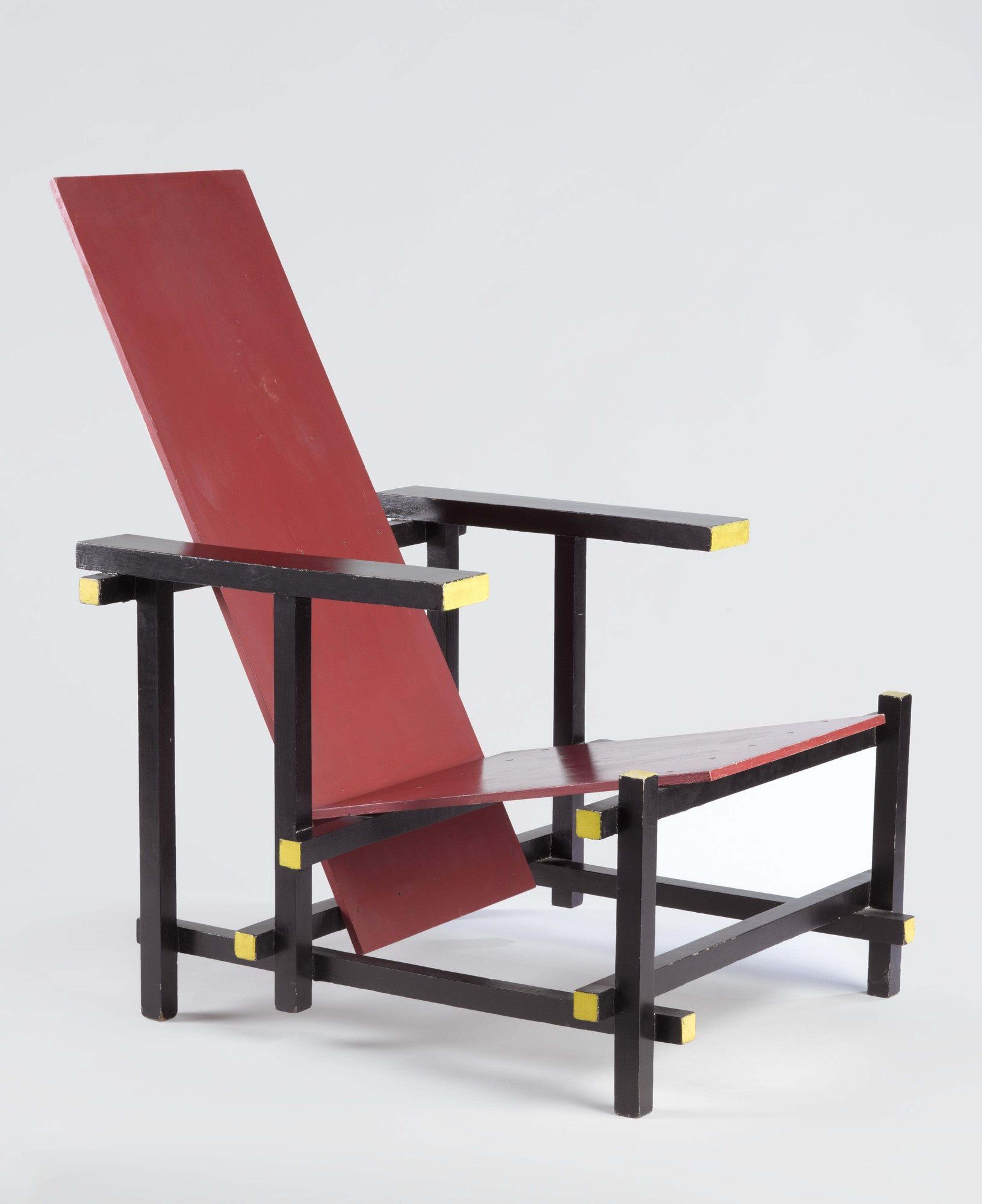 A chair made from straight pieces of wood arranged in geometric lines and painted black, red, and yellow