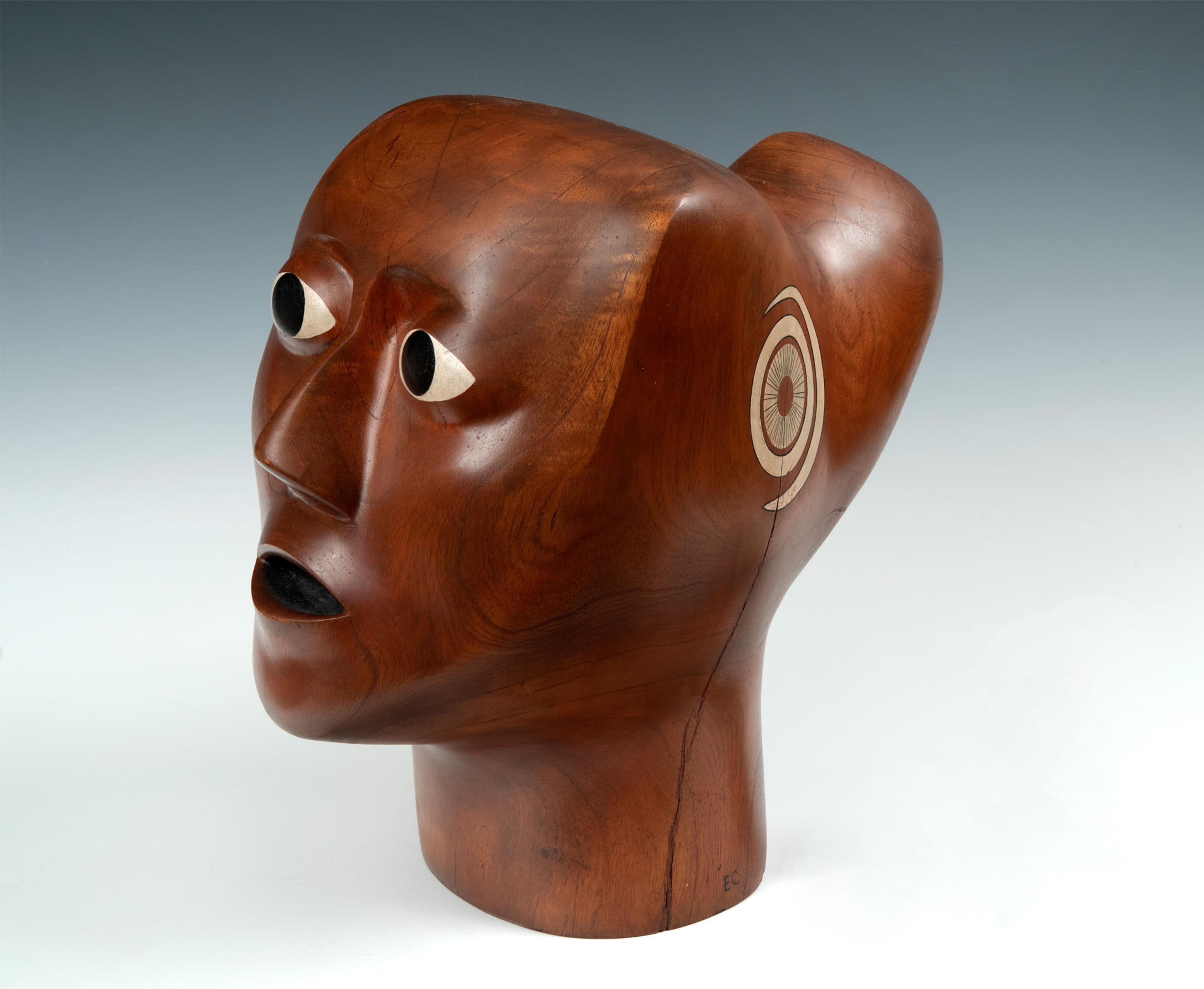 Wooden sculpture of a head set against a gradiant grey background