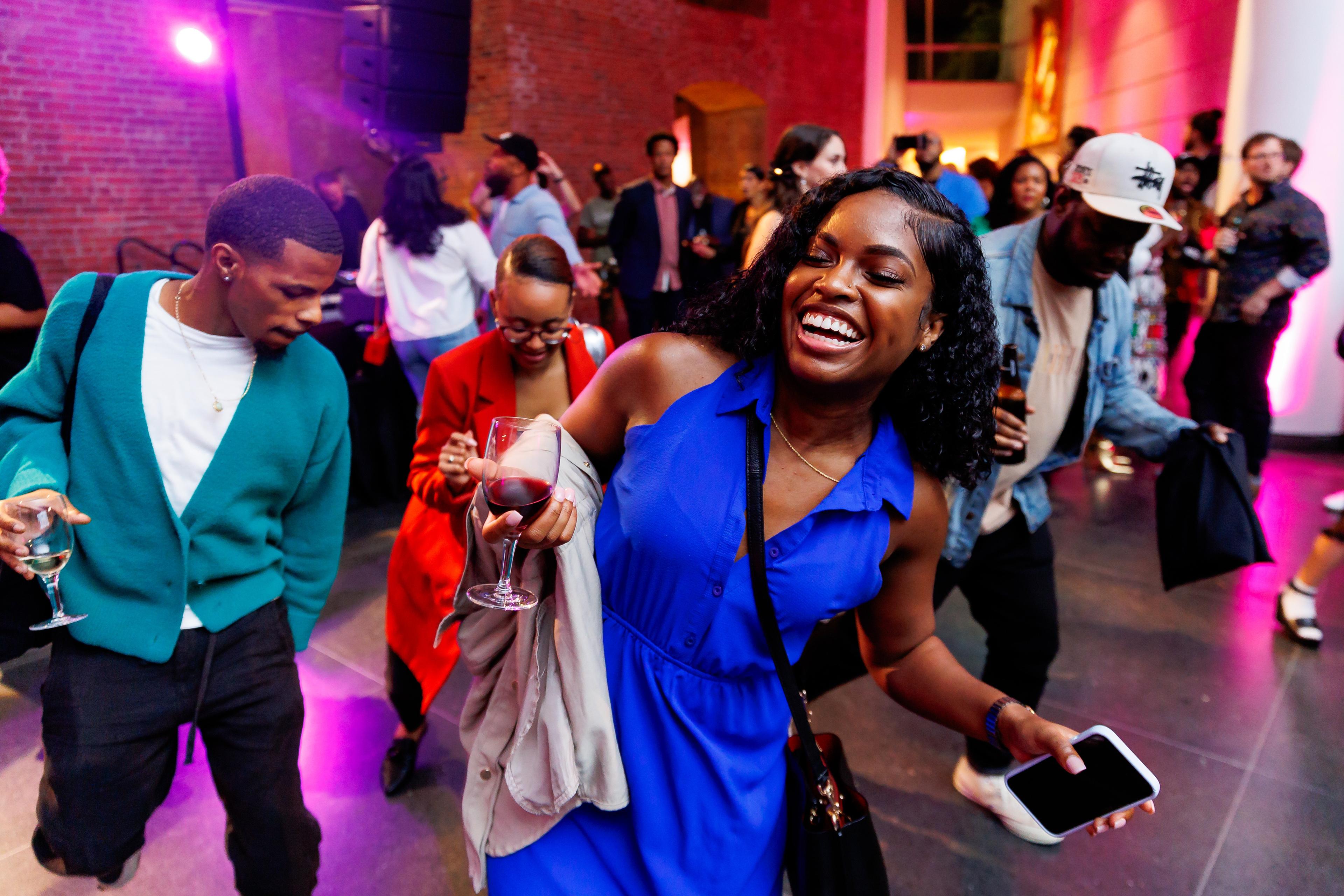 Partygoers dance under colorful lights in the Brooklyn Museum lobby