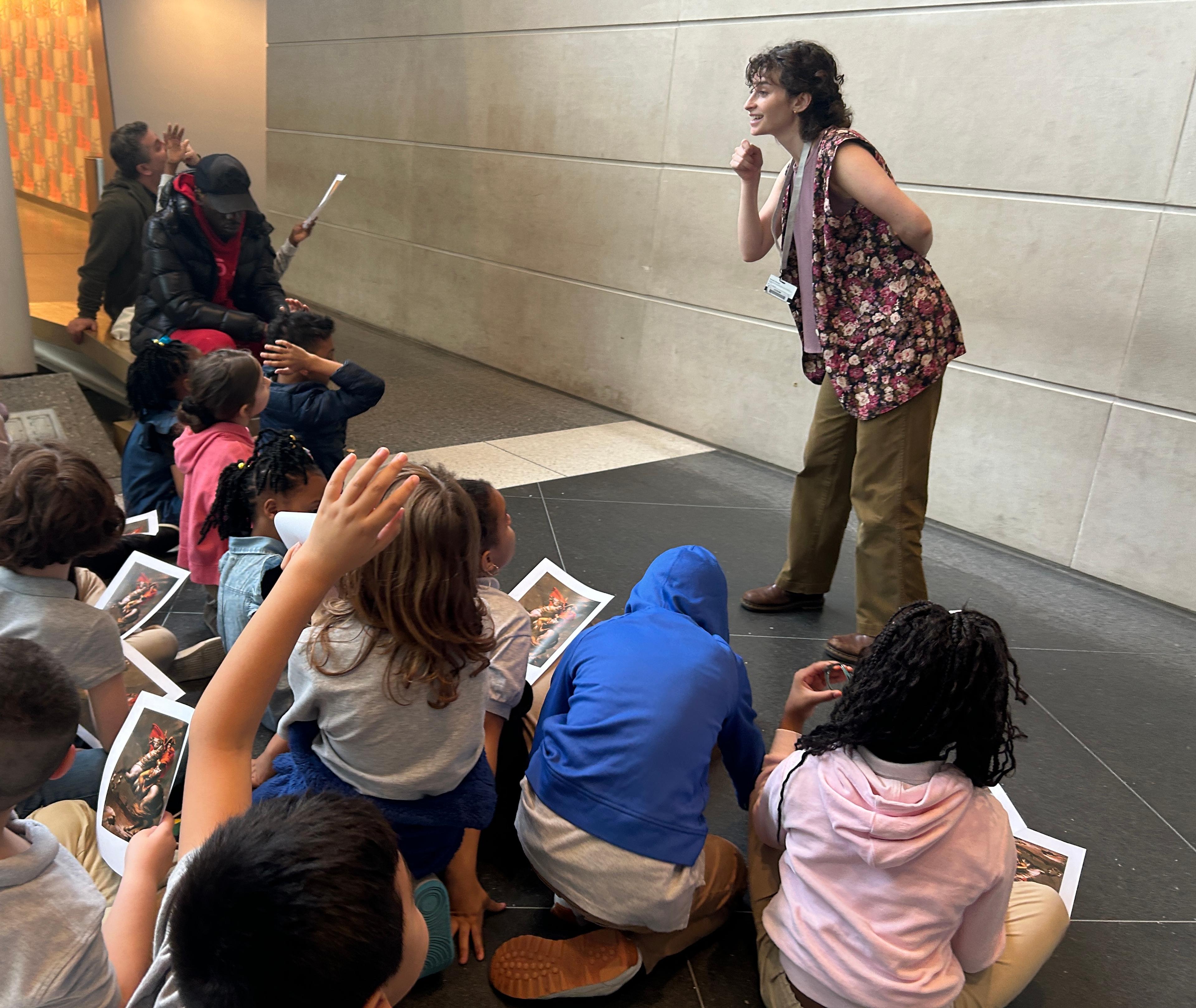 An adult instructor leads a seated class of young students