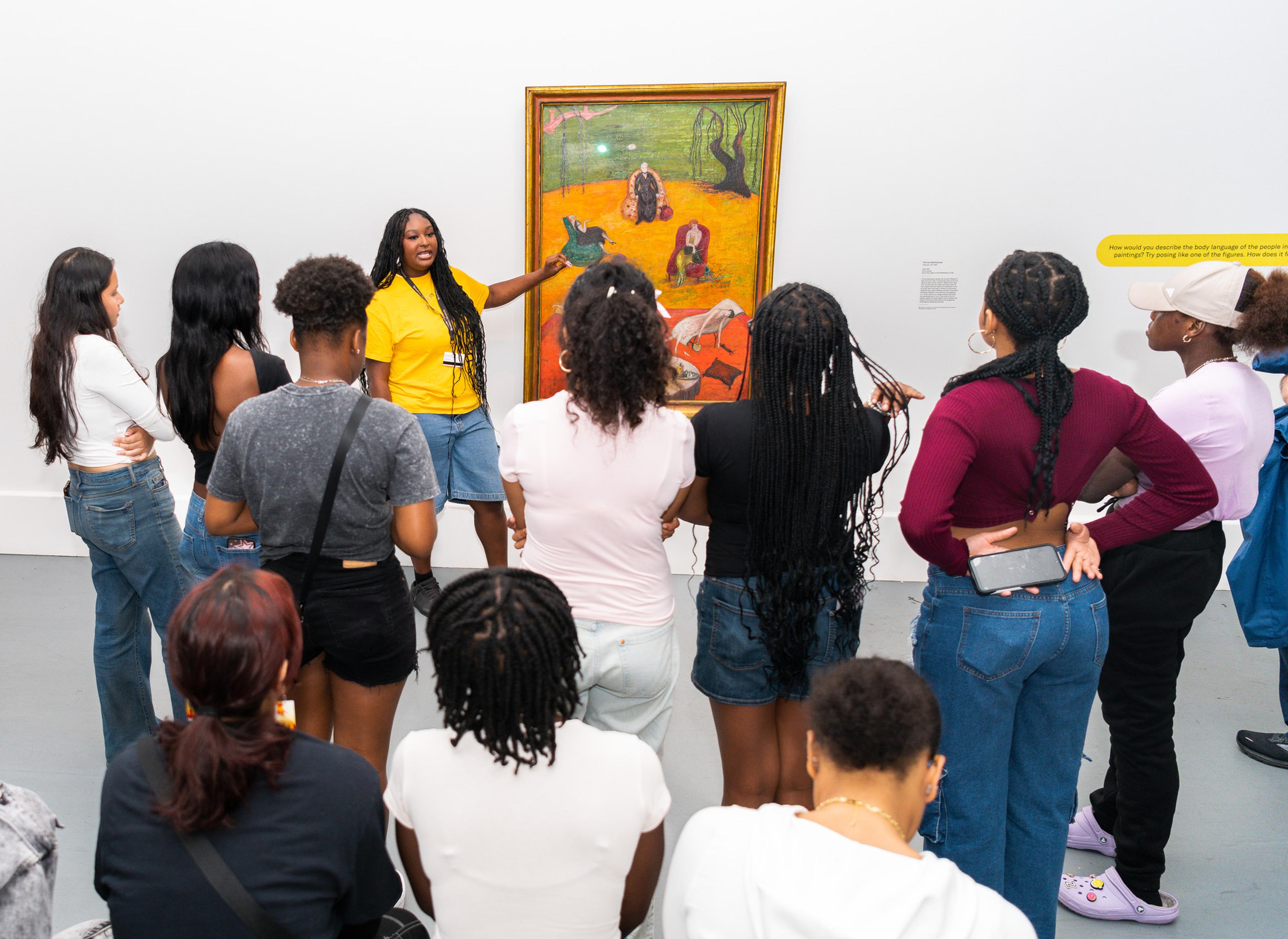 Gallery guide gestures toward a painting while a group observes attentively