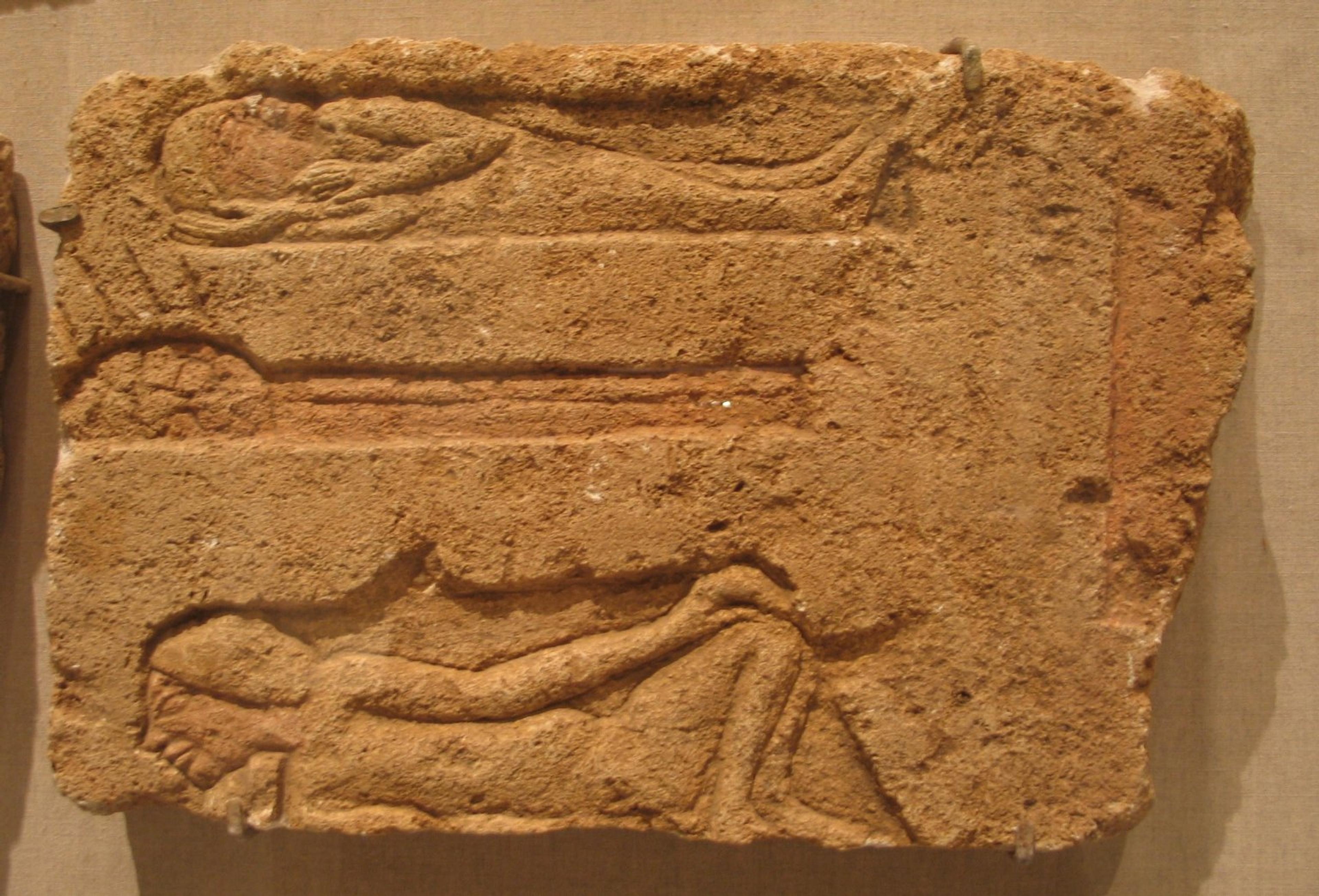 Carved relief showing two people laying under blankets around a fire