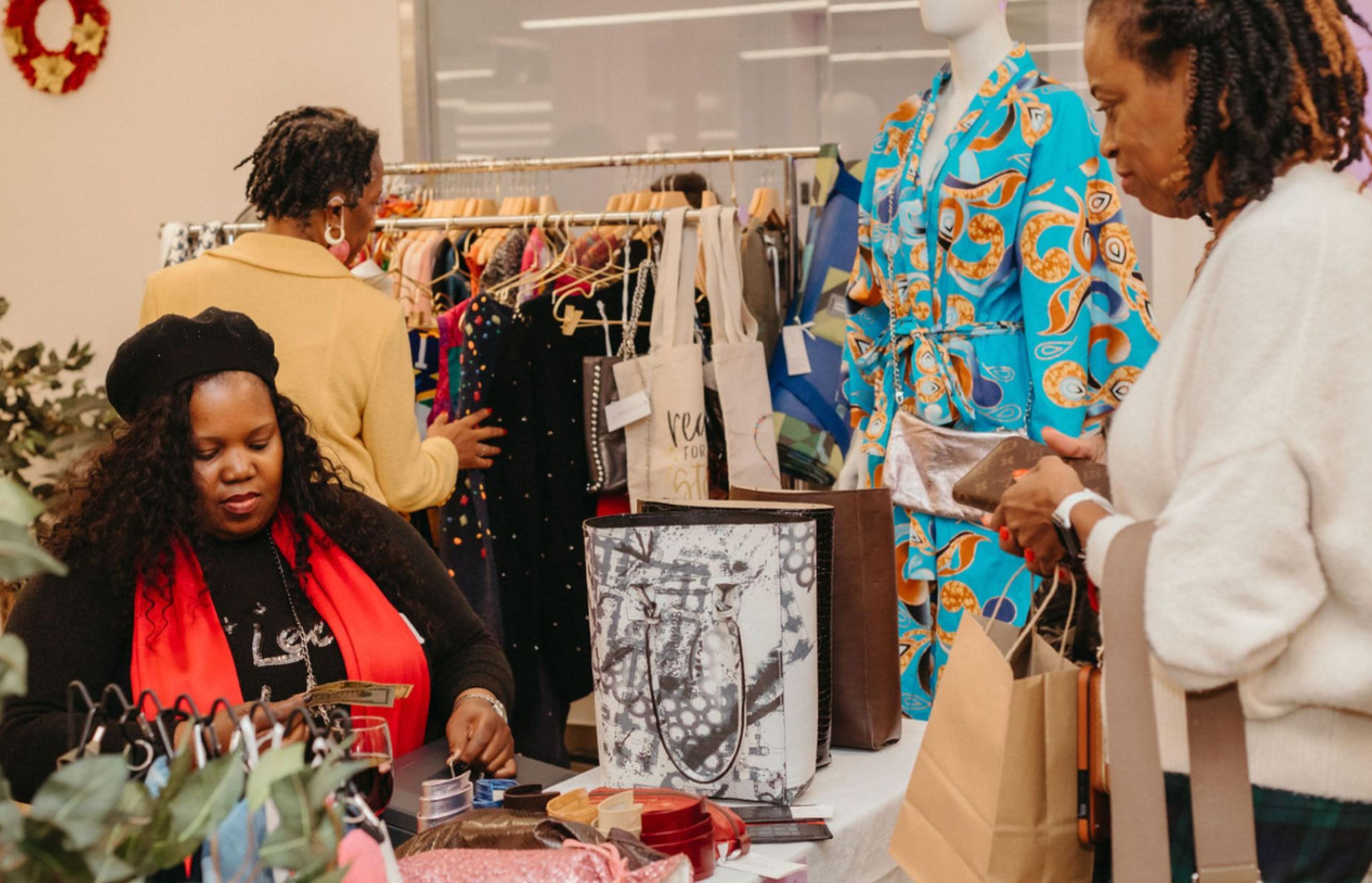 Customer purchasing an item from a seated vendor, with clothing rack in the background