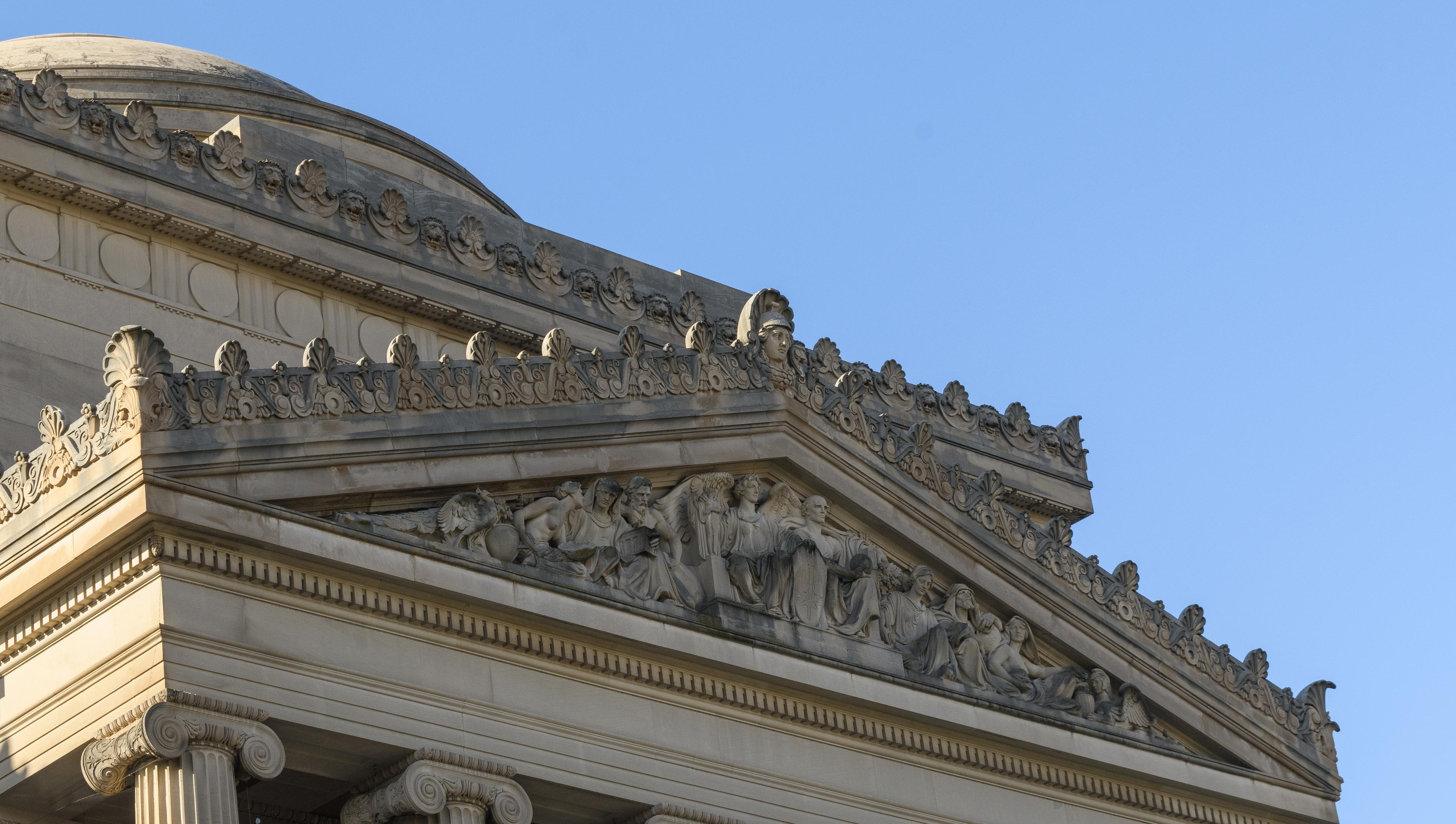 Architectural detail a buildng building, featuring a triangular relief, and a tip of a domed roof