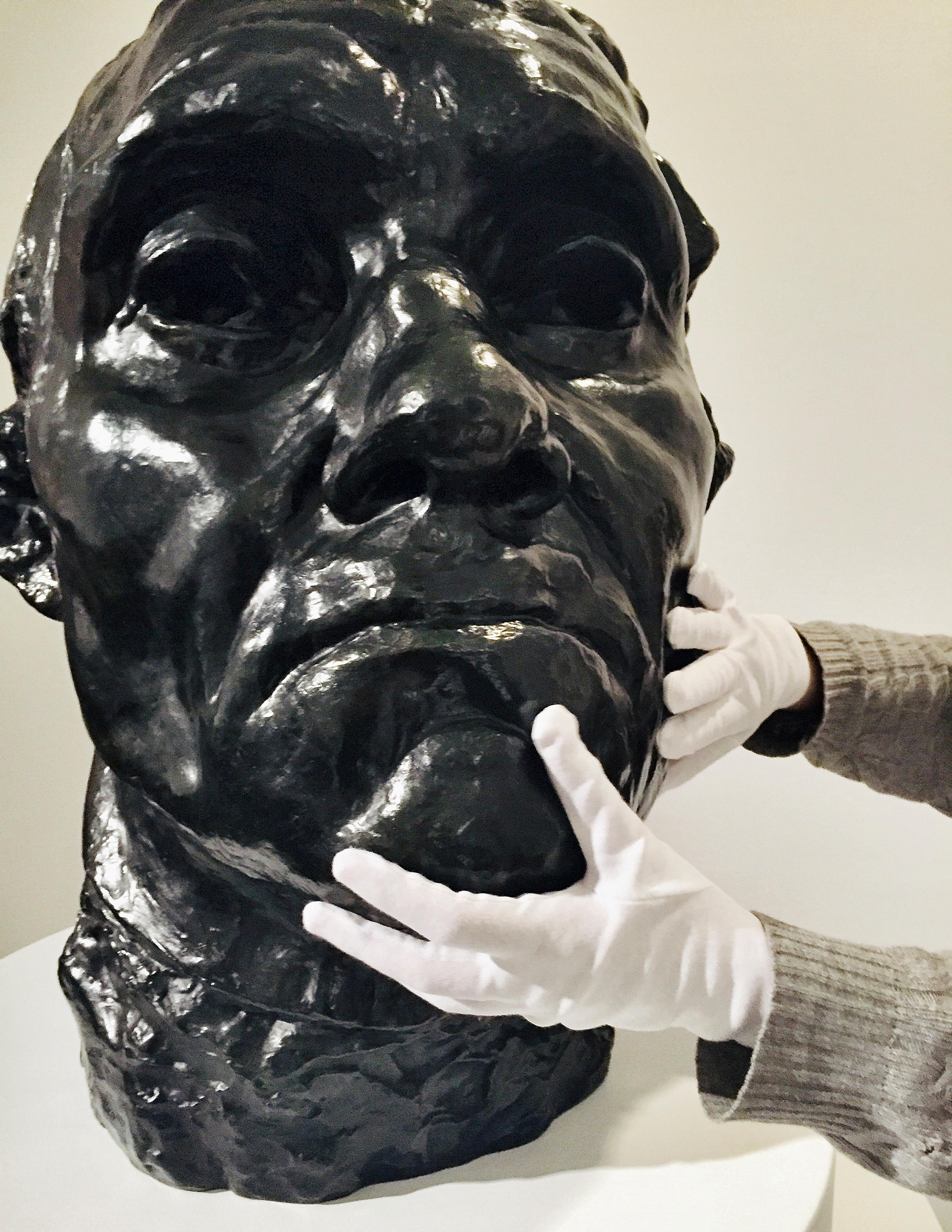 Two gloved hands touch Jean d'Aire, Colossal Head (Auguste Rodin (French, 1840–1917), ca. 1885, enlarged 1908–9; cast after 1971. Bronze, 251/2 x 213/4 x 201/2 in. (64.8 x 55.2 x 52.1 cm). Brooklyn Museum, Gift of Iris and B. Gerald Cantor, 1992.182). (Photo: Lindsay Londs Reuter)