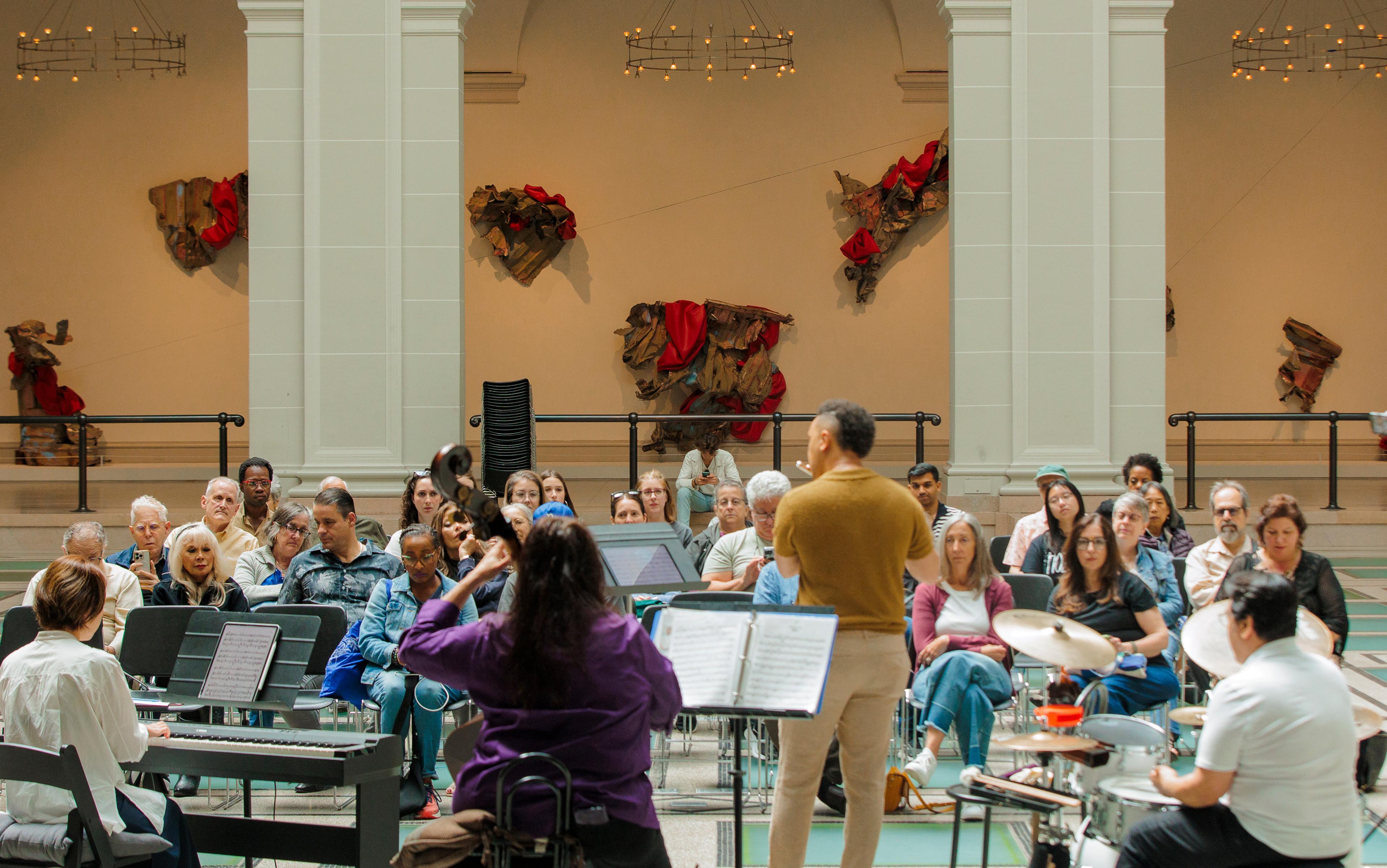 A group of five musicians play infront of an intimate crowd in the middle of a large gallery