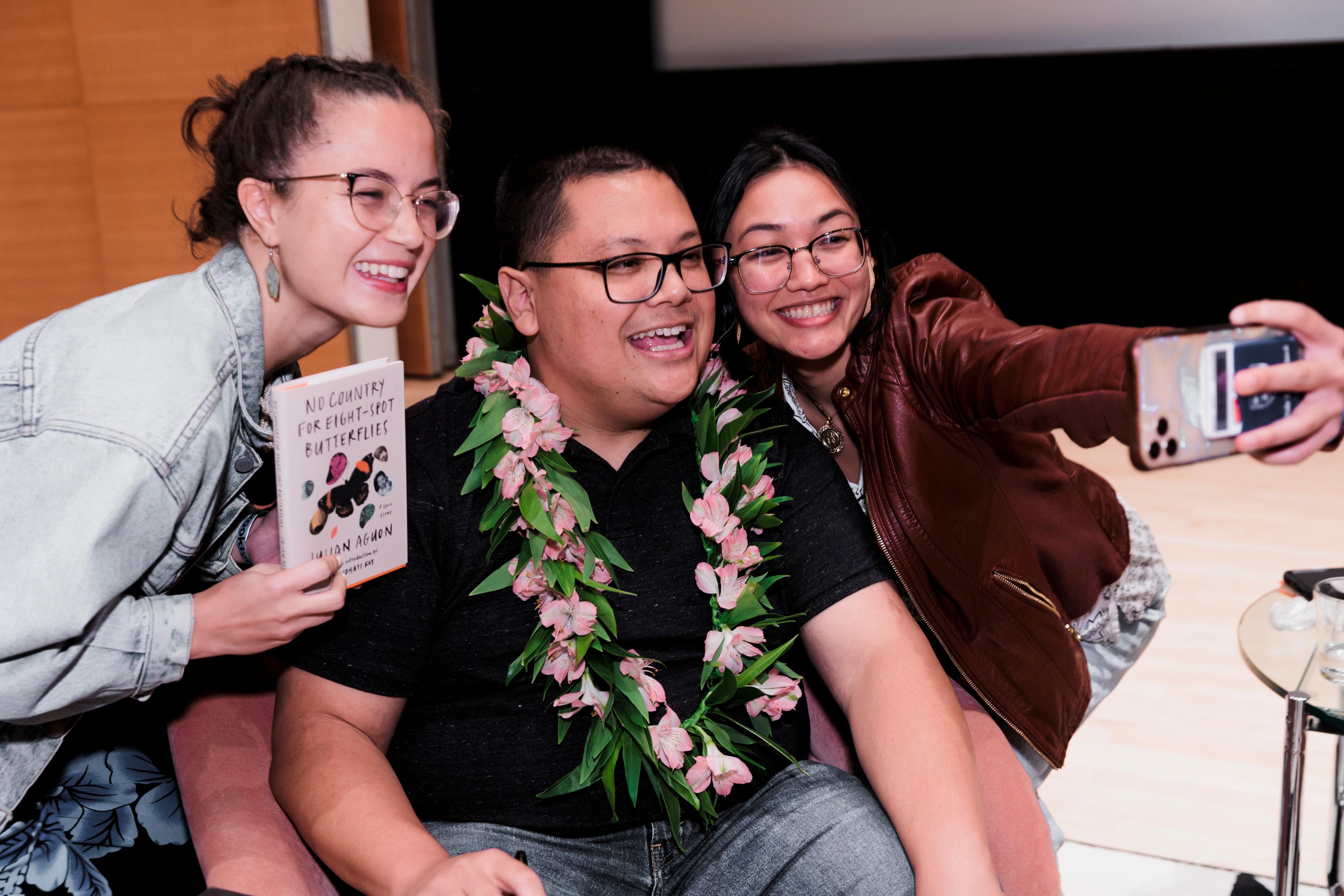 Three people taking a selfie on a stage, one holding a book