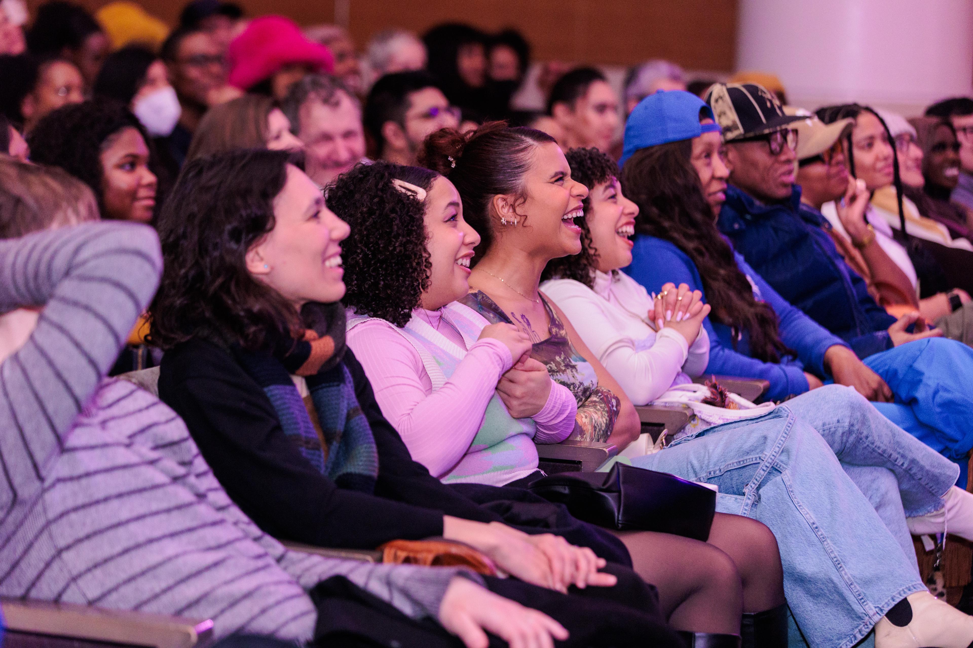 A crowd sitting in auditorium seat smiling and laughing