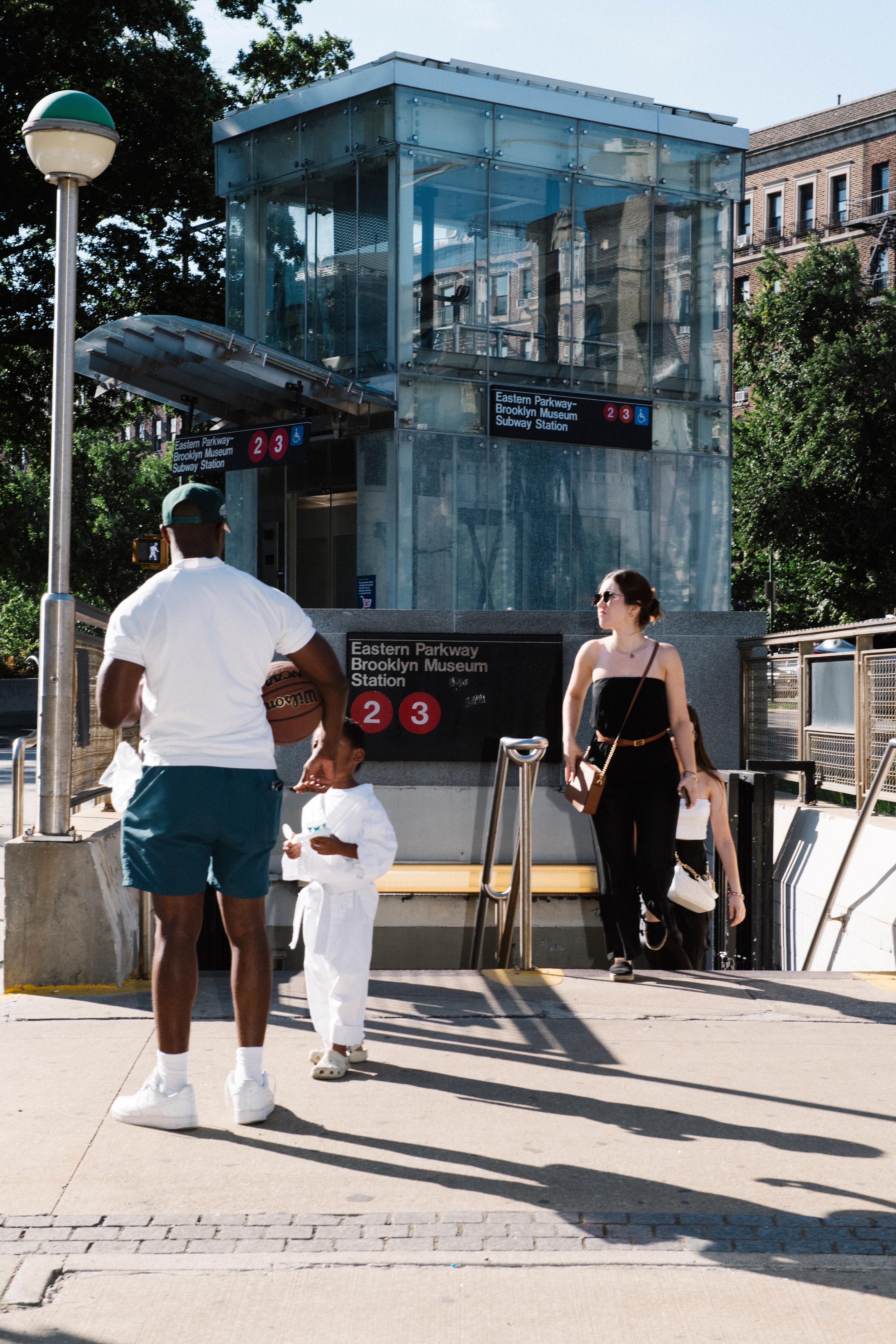 Three adults and a child walk out of a subway entrance that reads "Eastern Parkway–Brooklyn Museum Station 2 3"