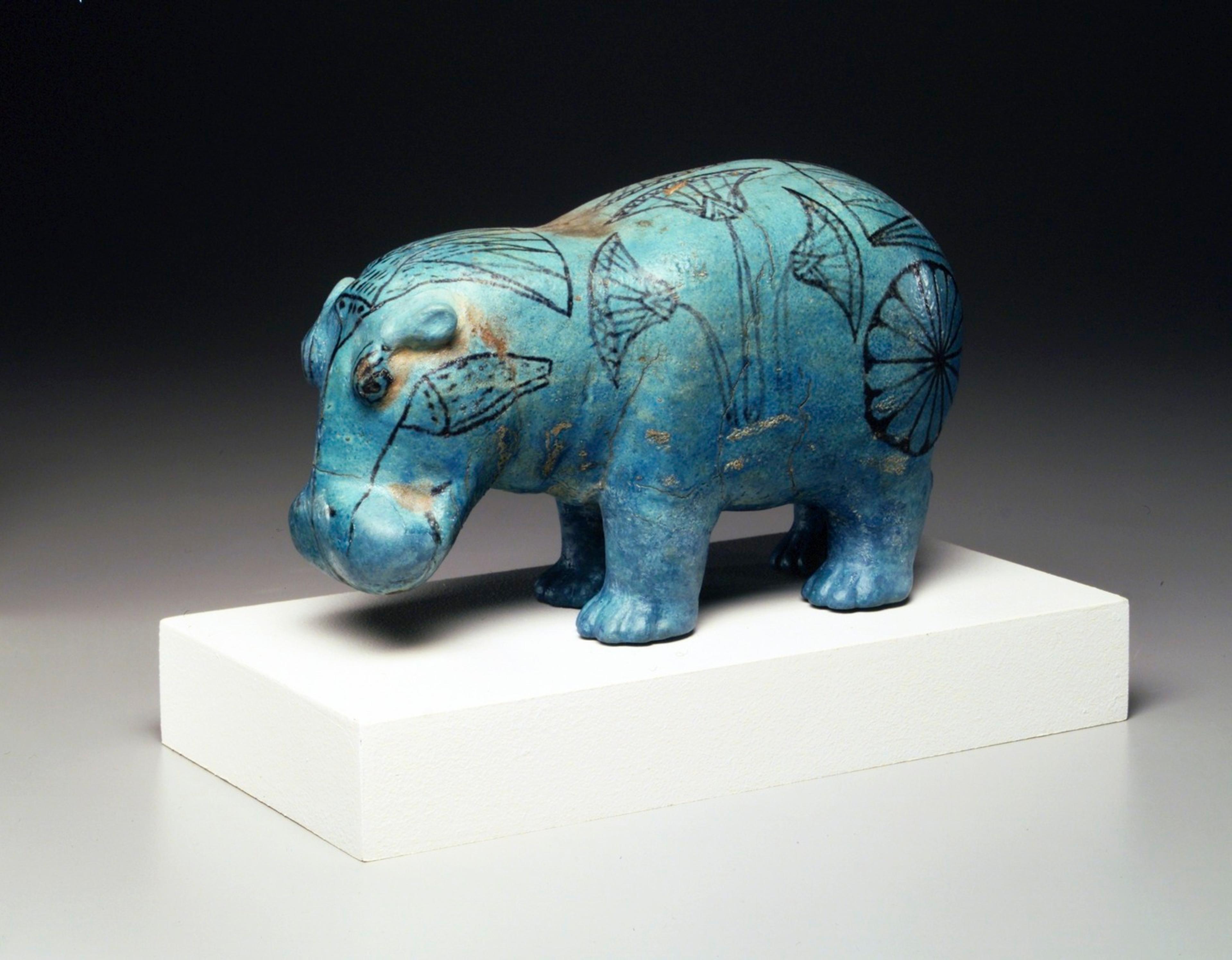 A sculpture of a hippopotamus colored turquoise-blue and decorated with lotuses drawn in black