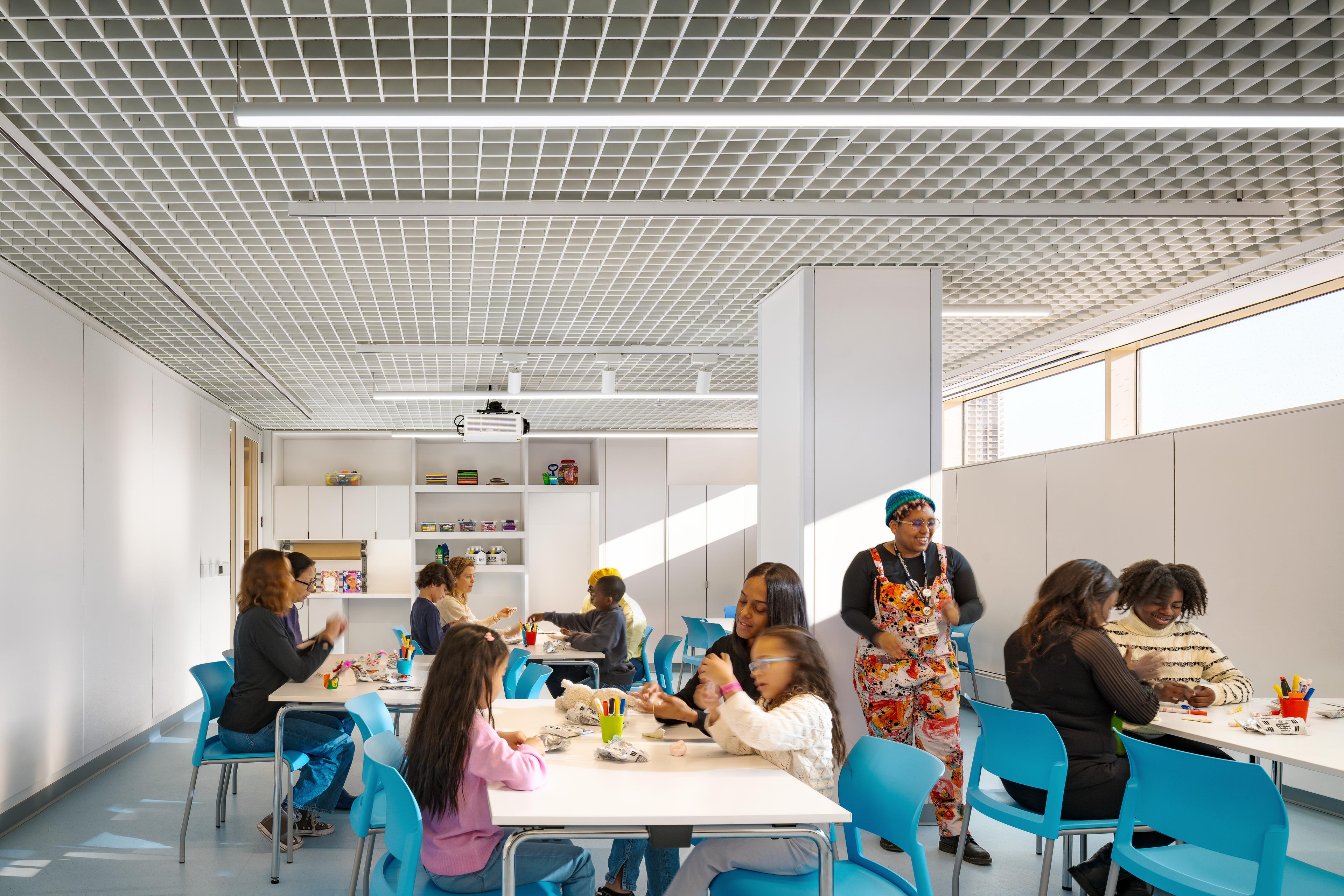 Classroom of students of all ages work on art projects while a teacher looks on smiling