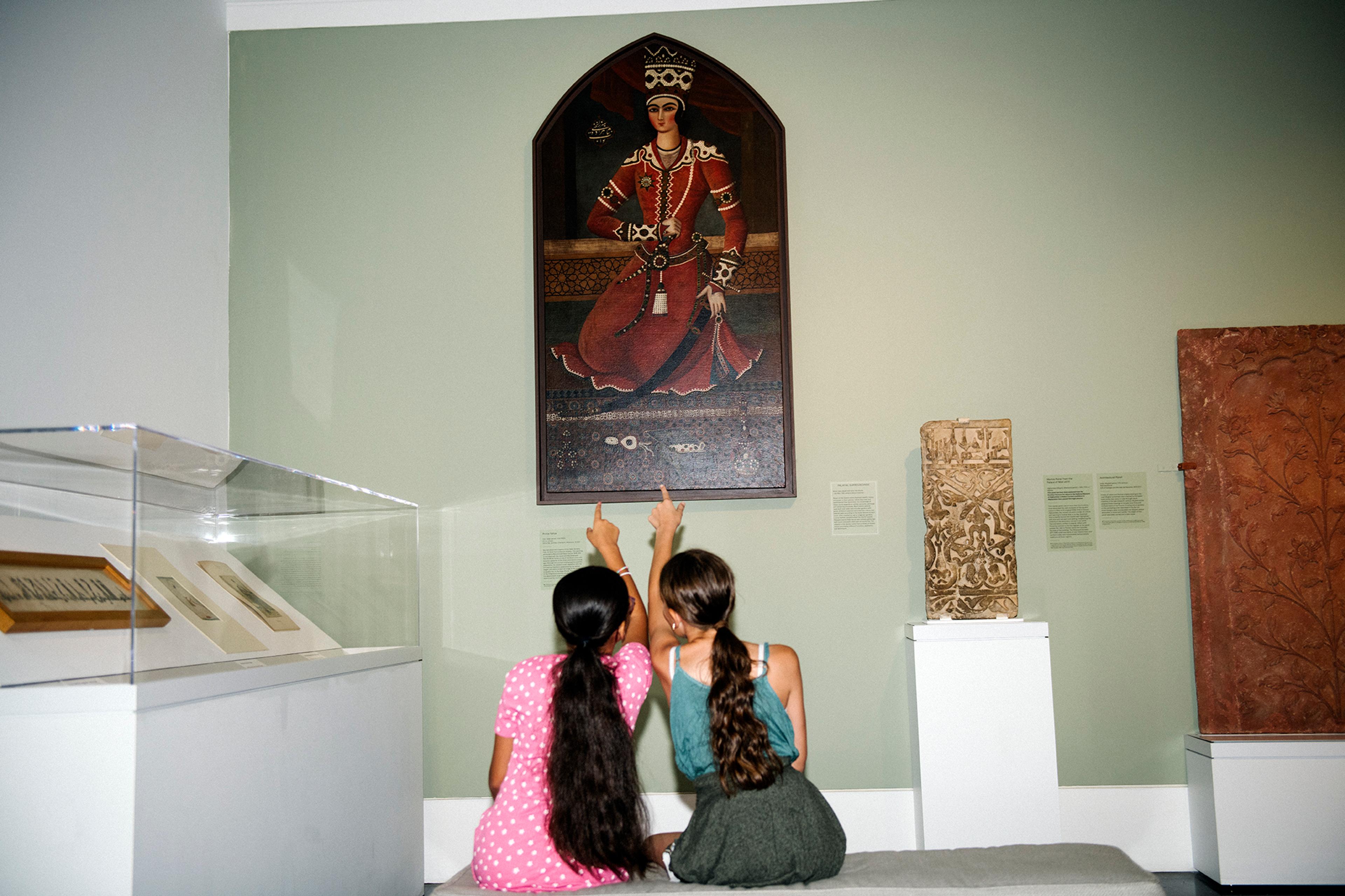 Two children sitting in a gallery, pointing at an artwork