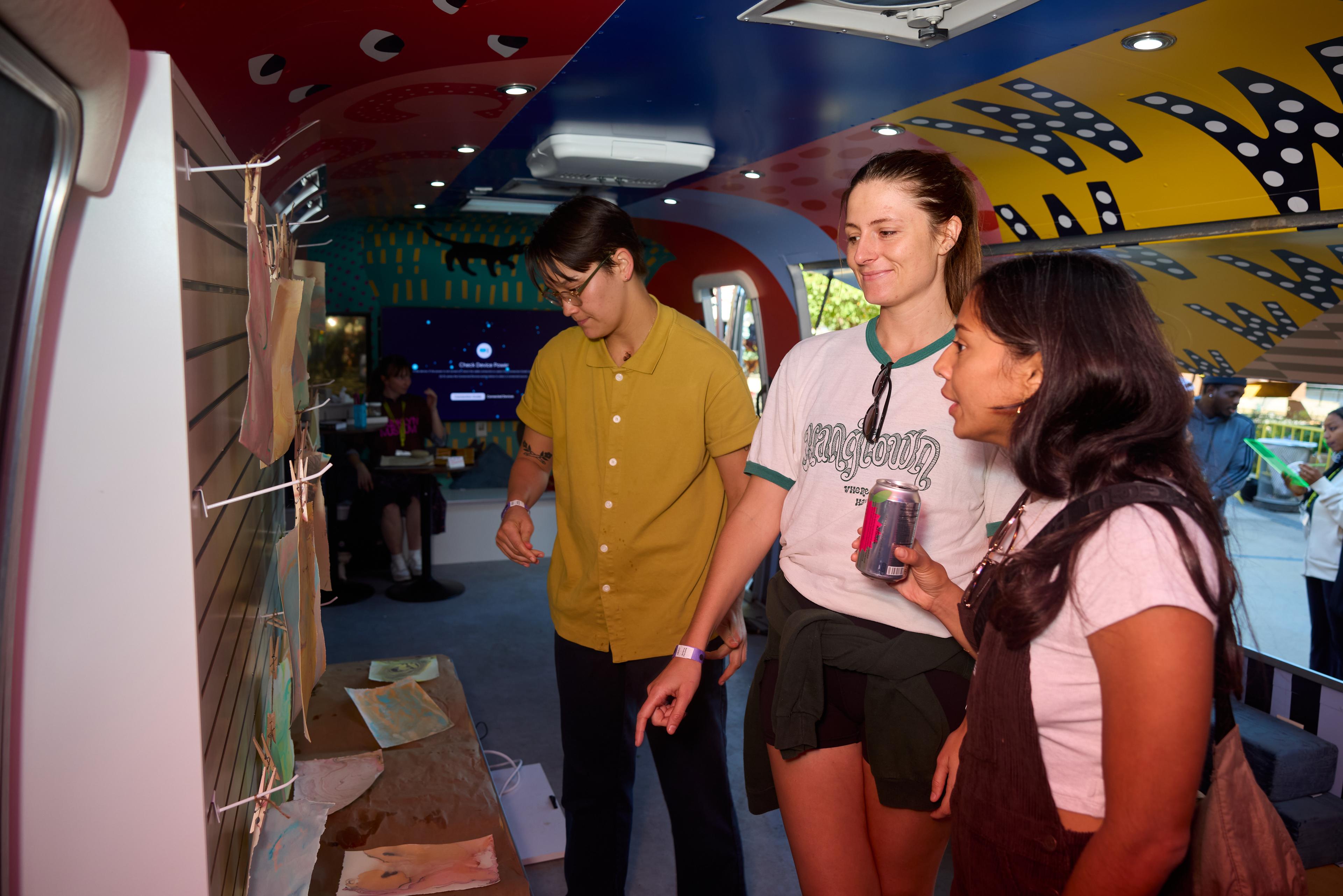 Three people looking at artworks in an Airstream trailer