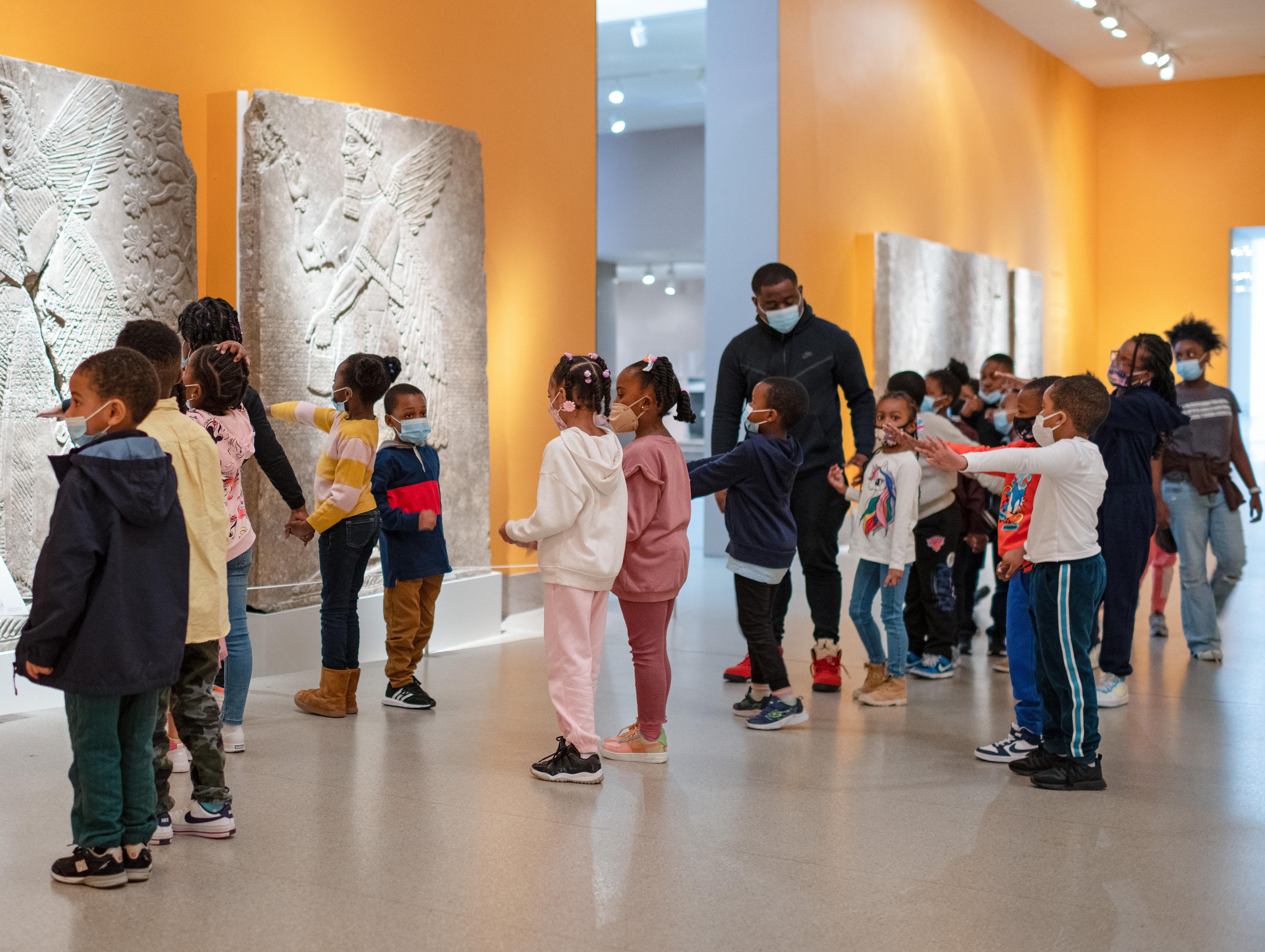 A teacher guides a group of young educators through a yellow gallery filled with ancient Assyrian reliefs