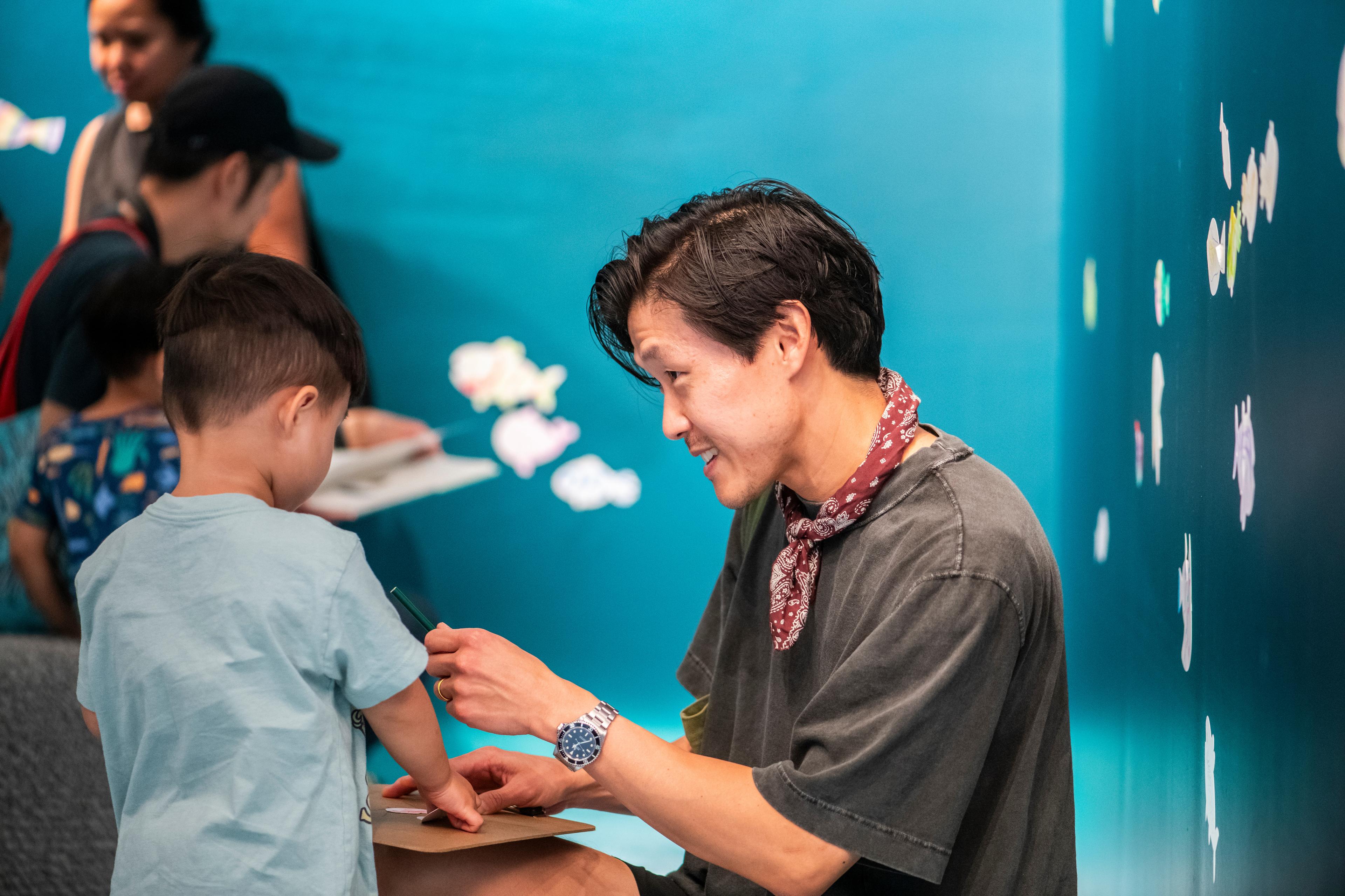 A man kneeling and handing a child a colored pencil