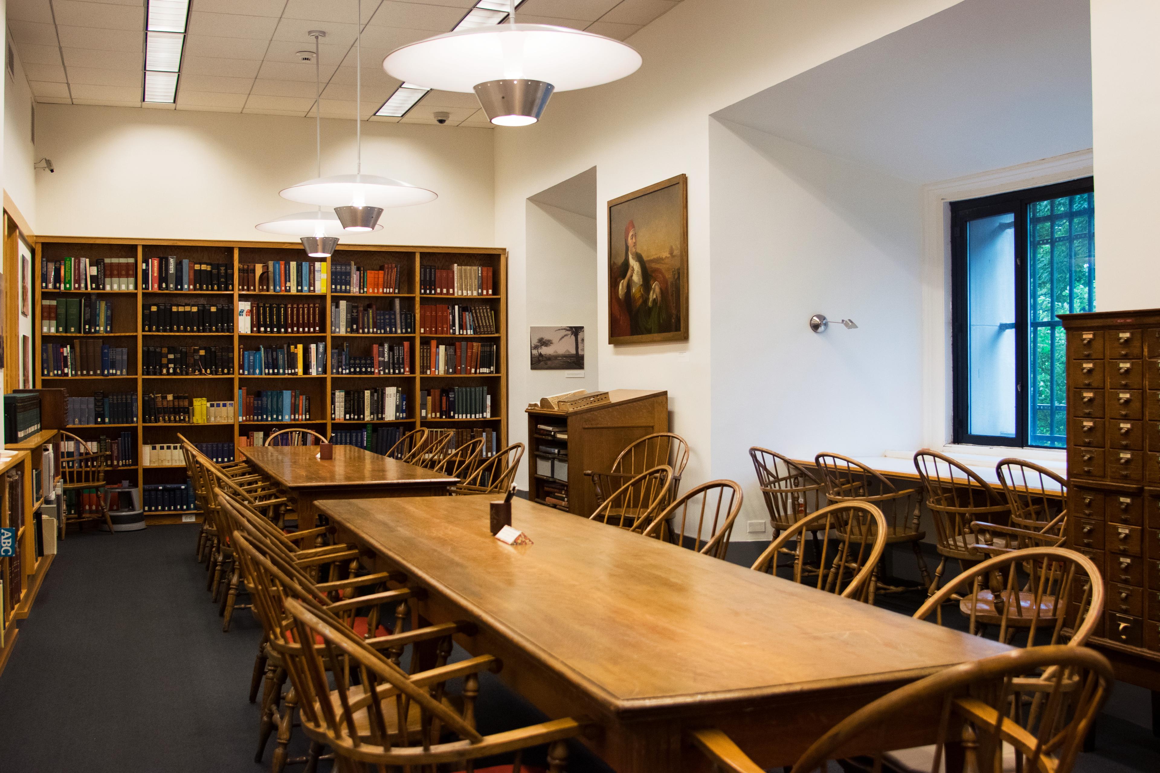 Long tables with many wooden chairs in the center of a room lined with book shelves and card catalogues