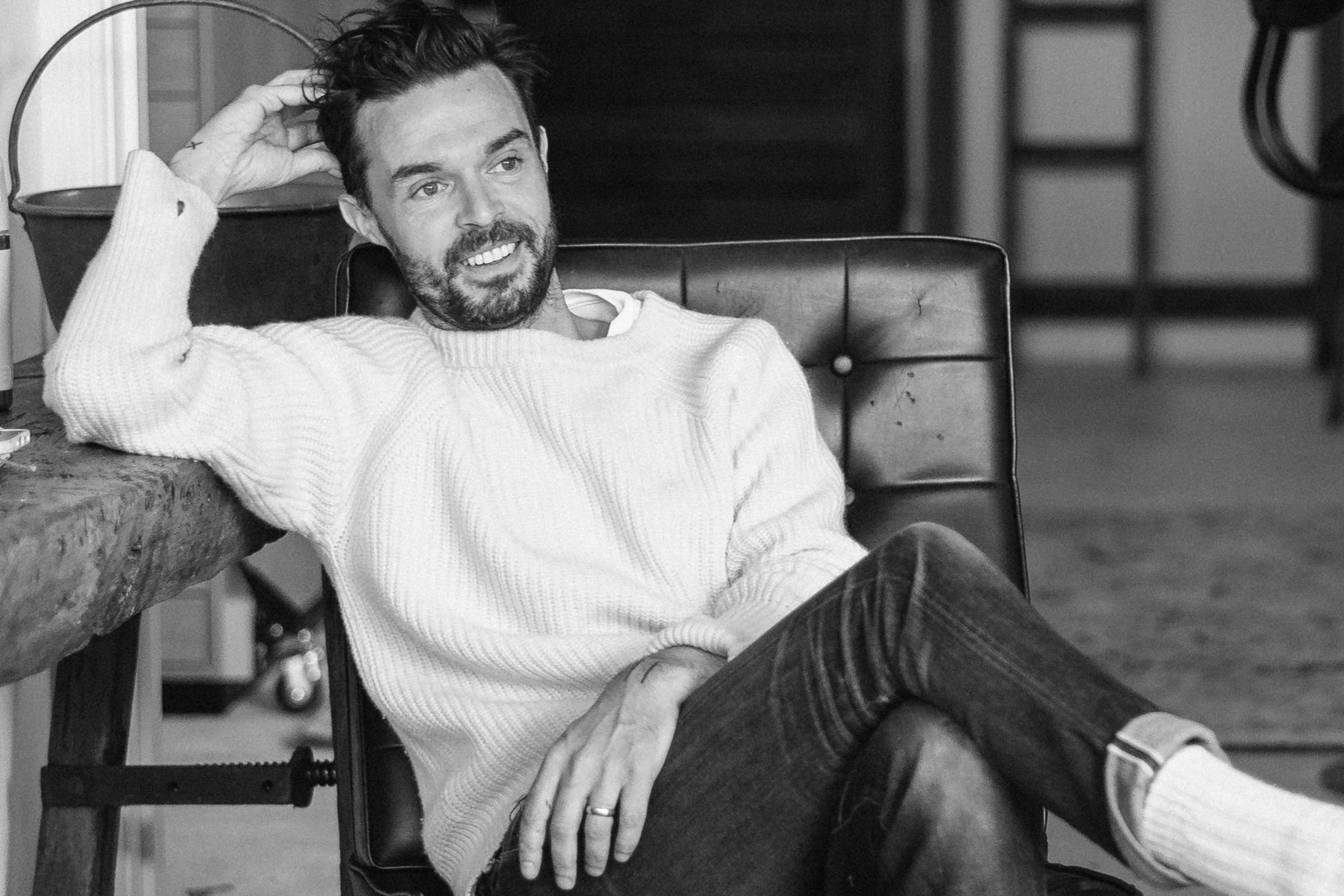 Black-and-white photograph of a person in a leather chair wearing a sweater and jeans