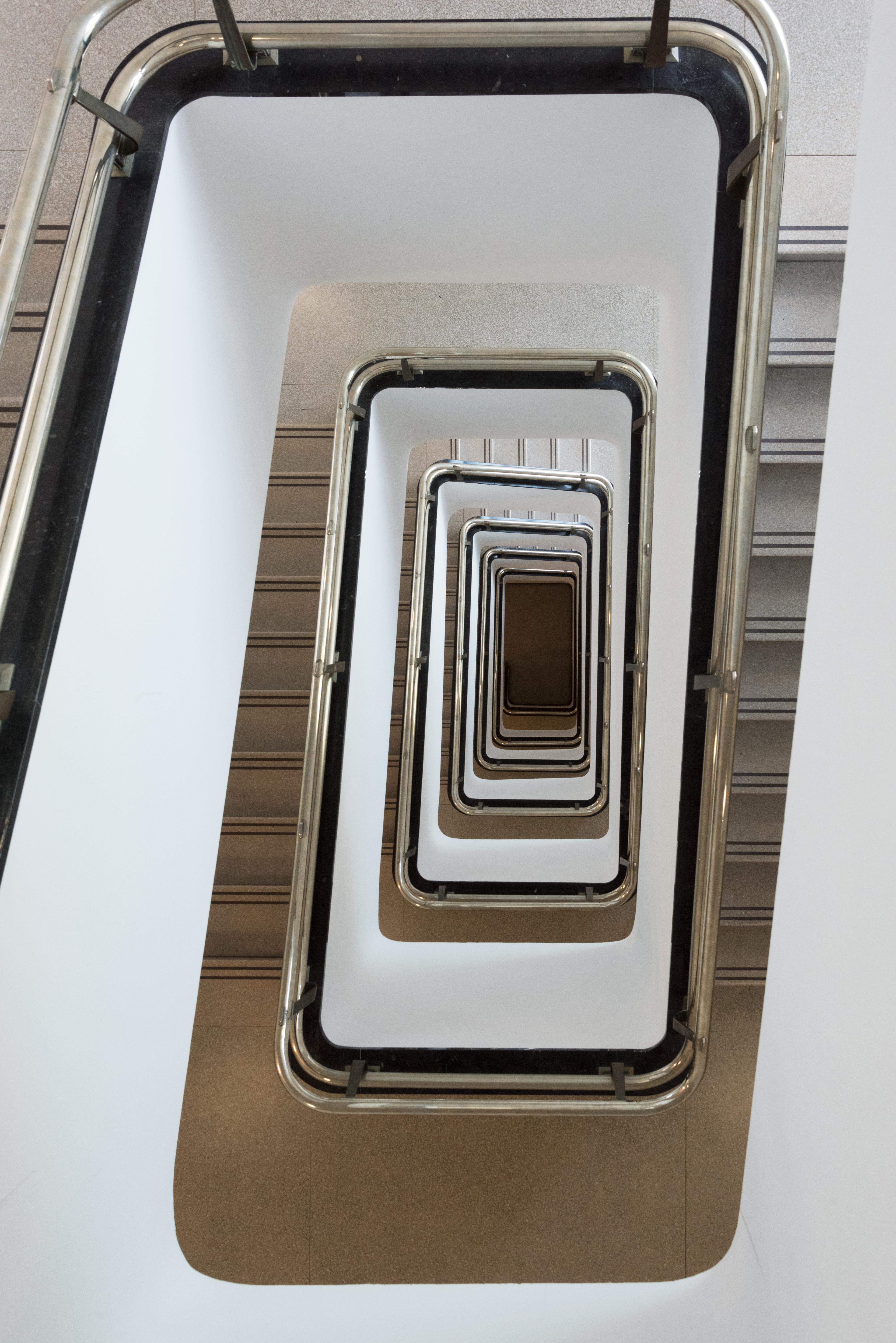 Photo of a spiral staircase with white walls, grey floors, and silver handrails