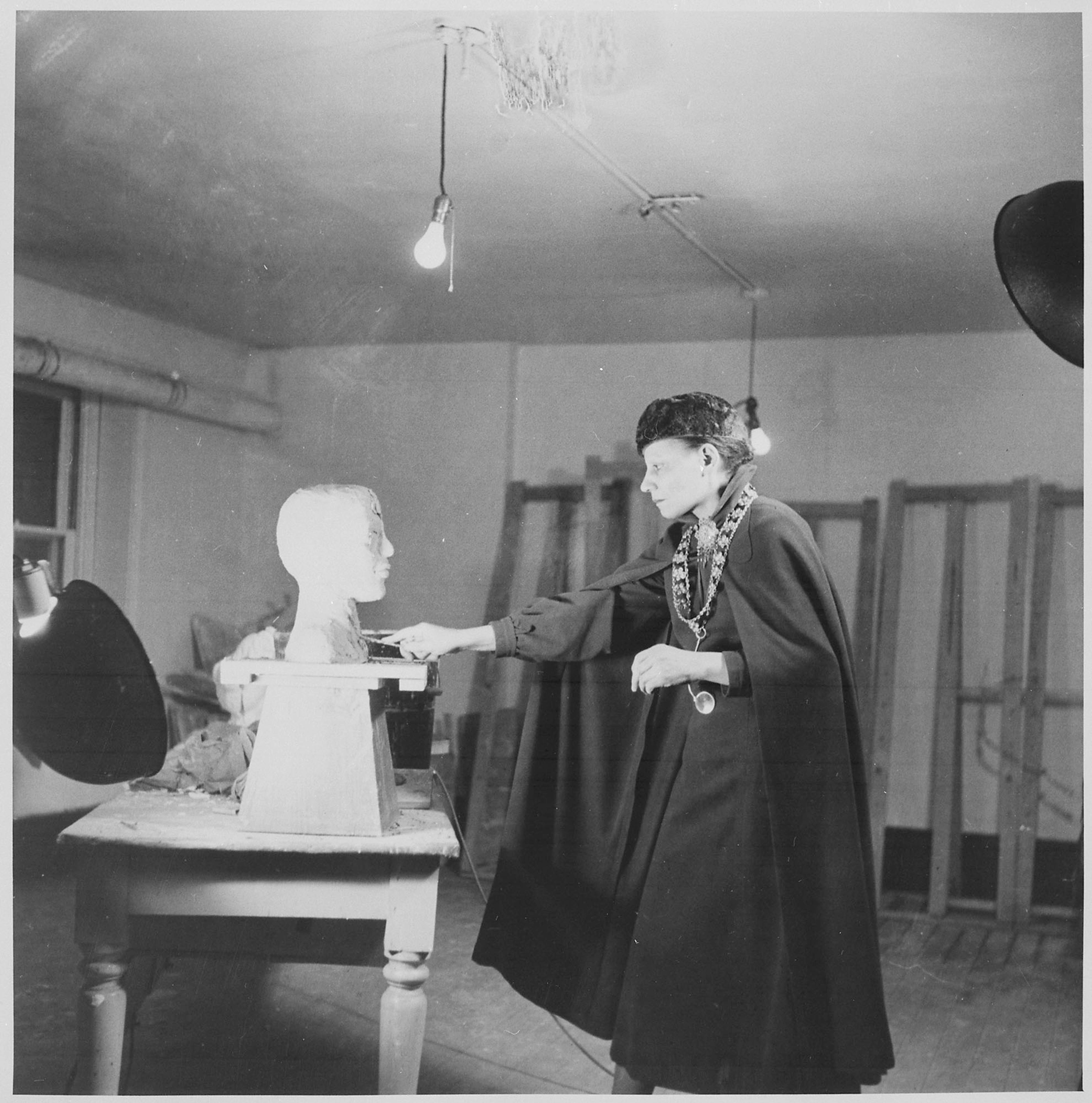 Artist in a dark cape sculpting a bust in a studio