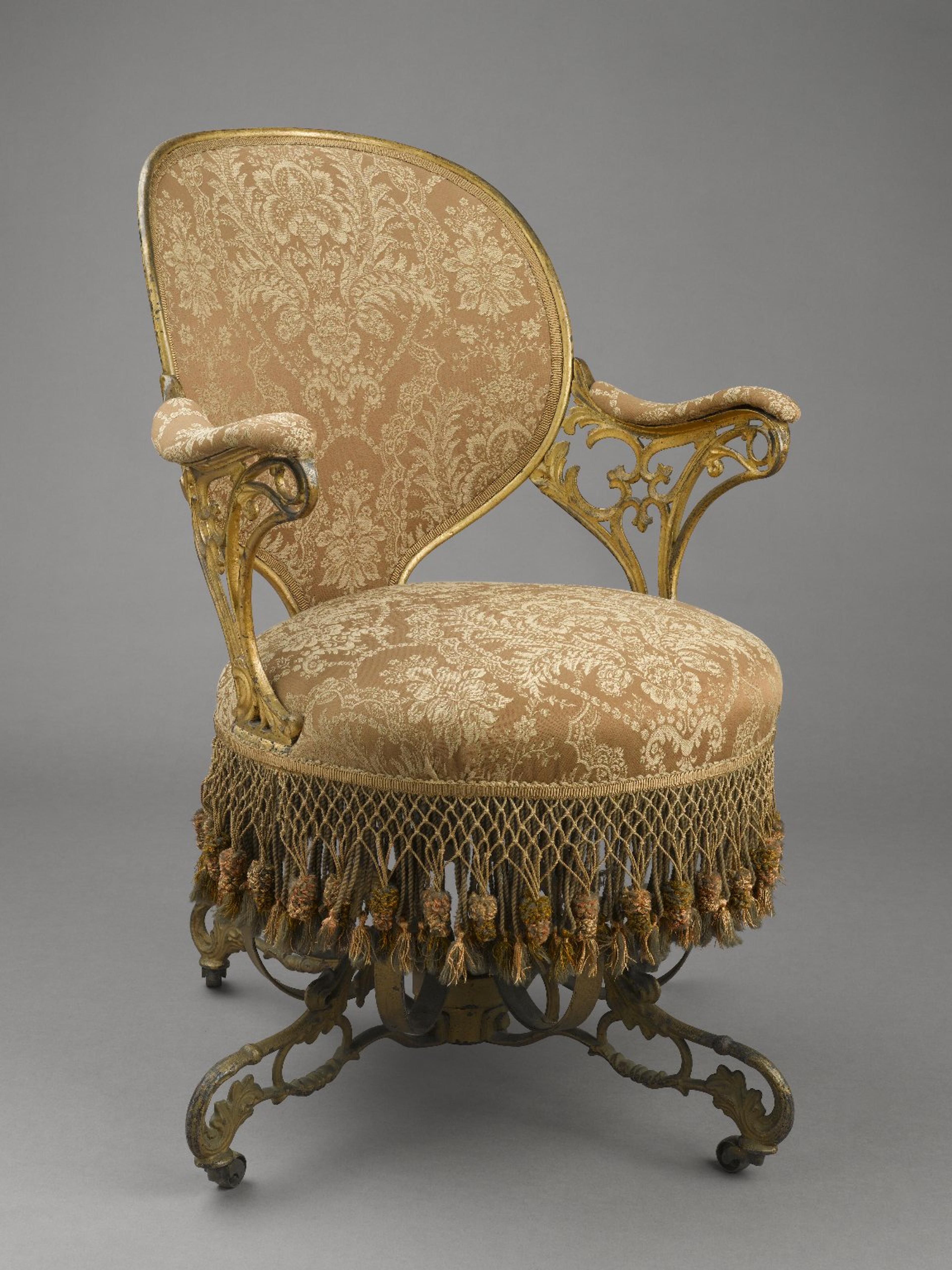 An ornate armchair with a gilded frame, intricate upholstery, and fringe tassels