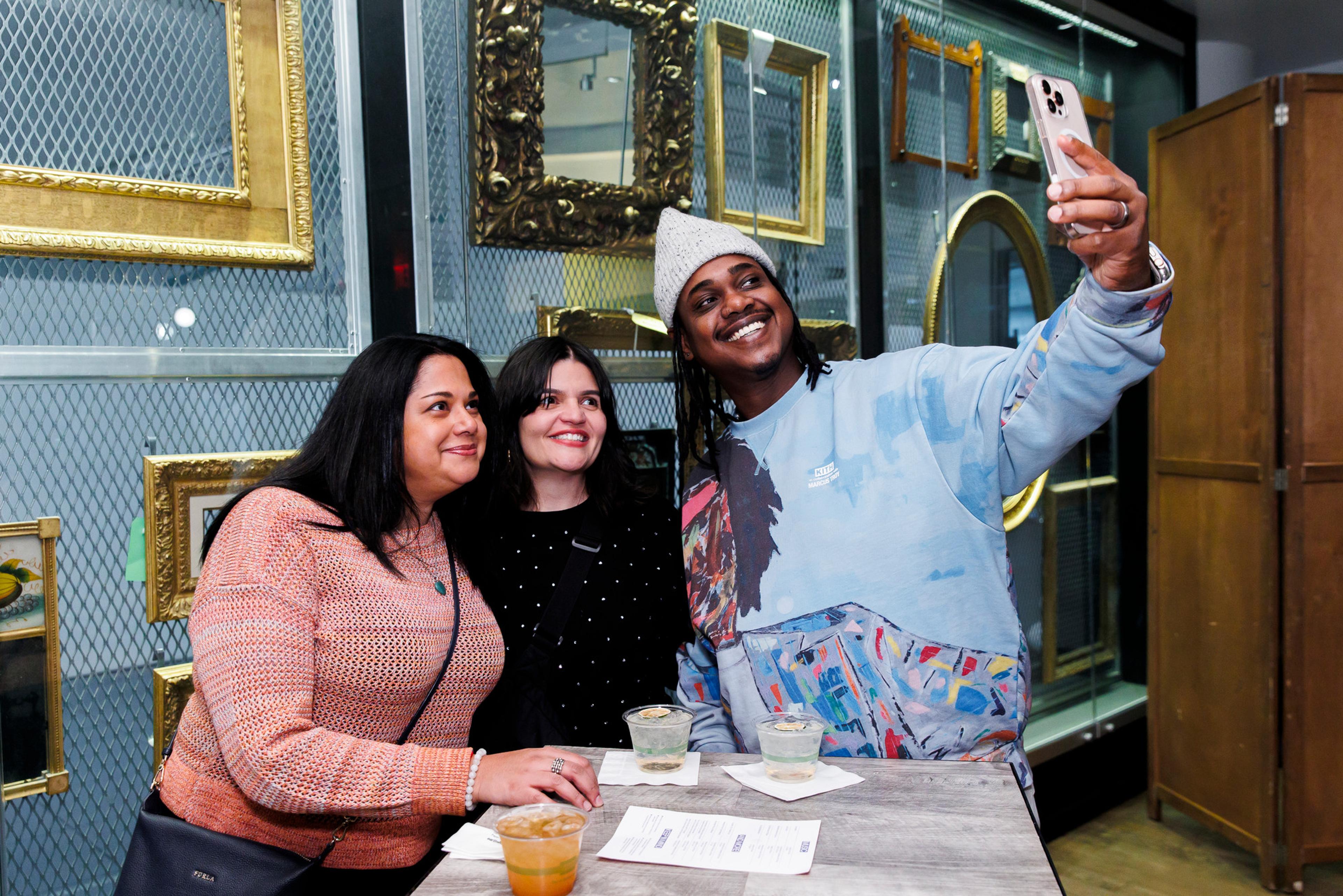 Three people posing for a selfie in front of a wall of gilded frames