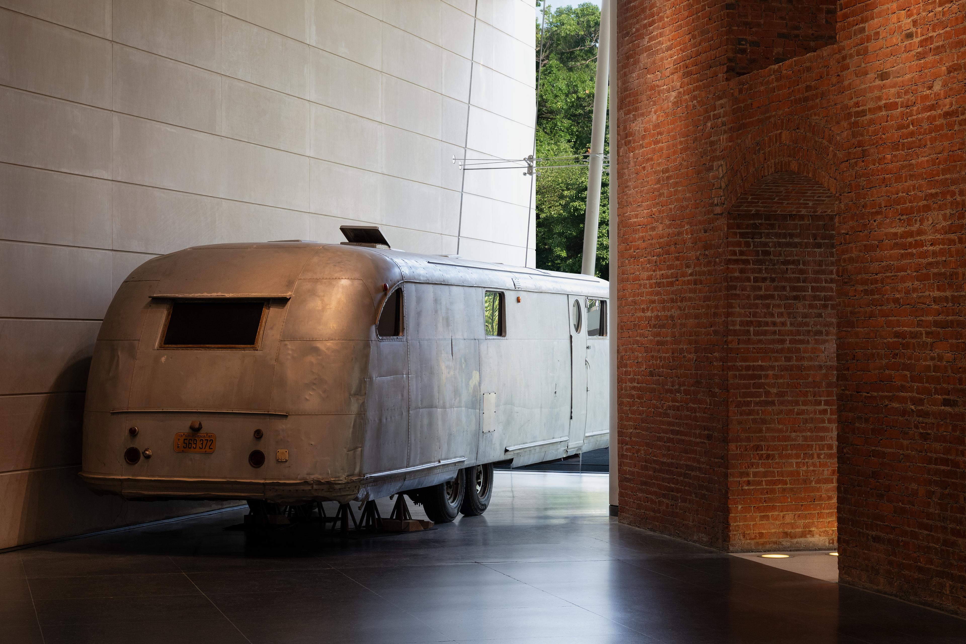 Exterior view of a trailer parked between a concrete wall, a large glass window, and a brick wall.