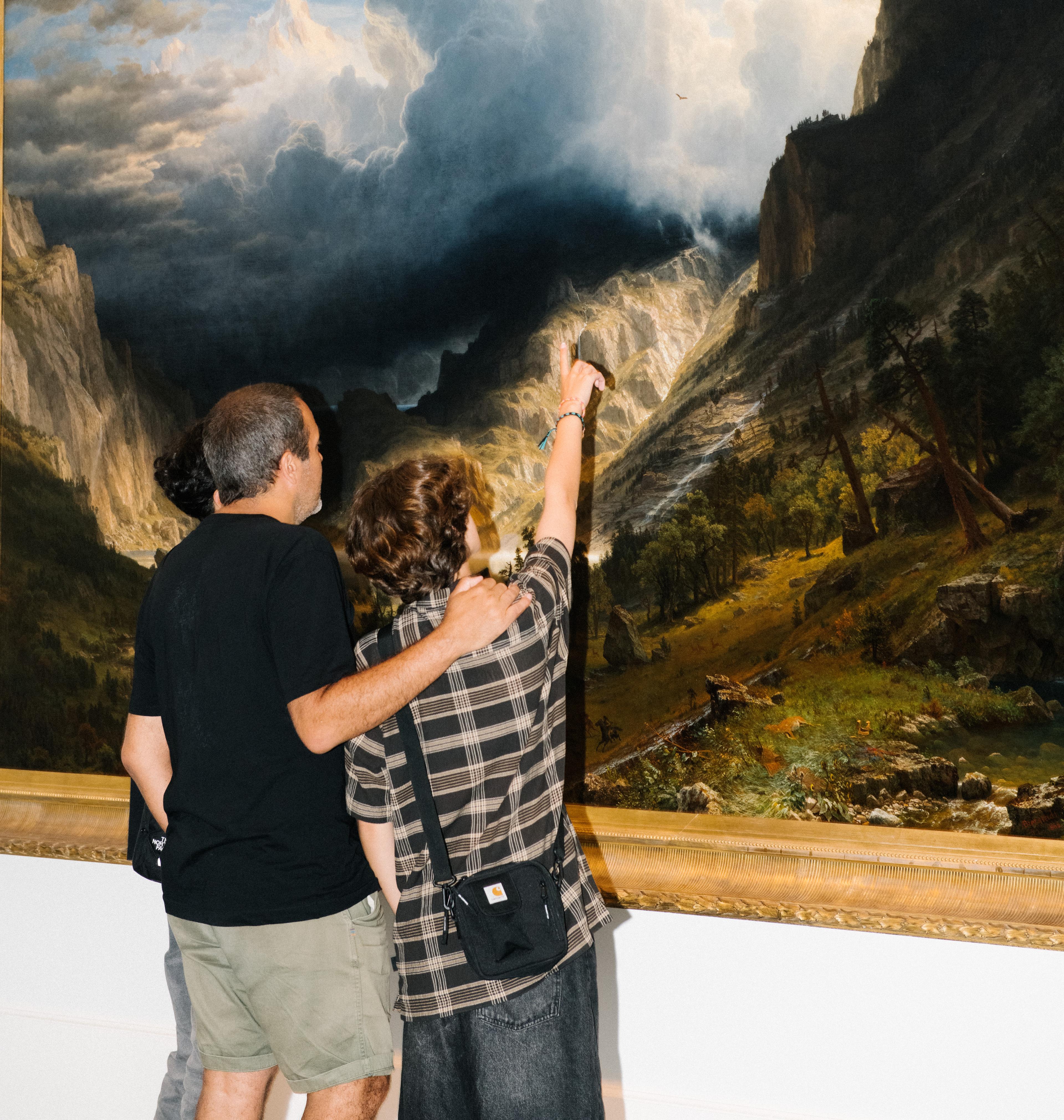 Family of three looks at a large stormy landscape, one of them pointing up towards the clouds