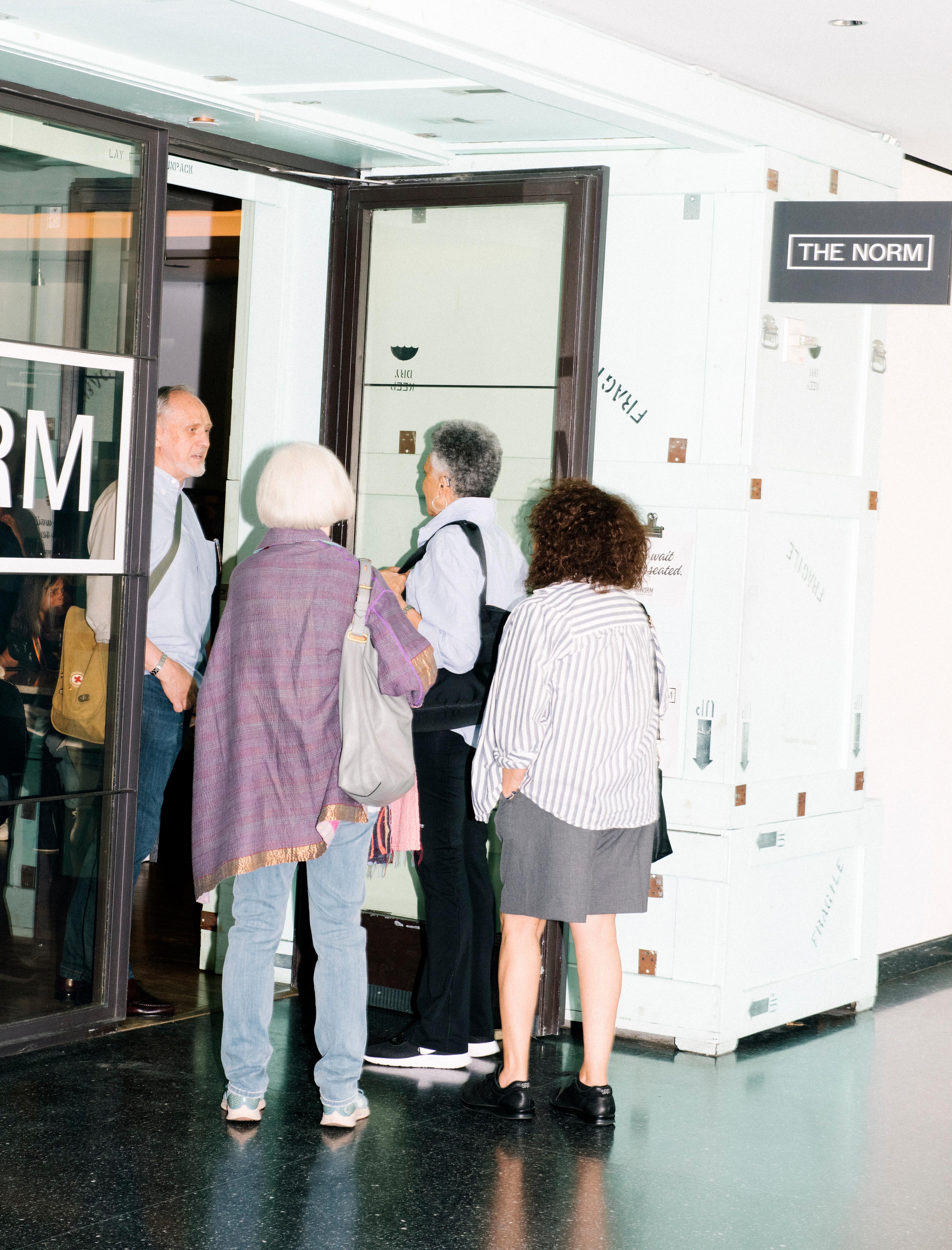 Four adults lined up at a restraurant entrance under a sign that reads "THE NORM"