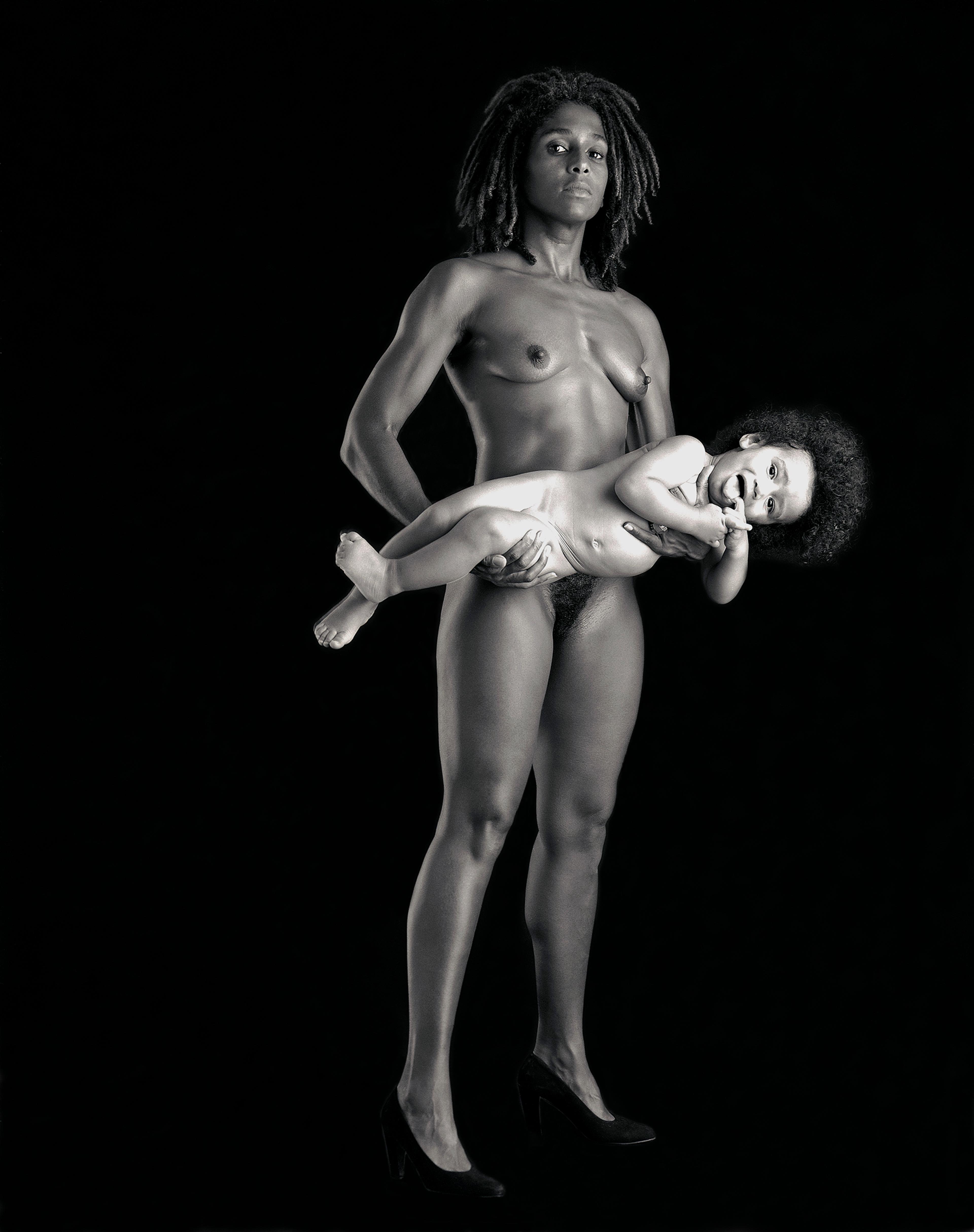 A black-and-white photograph of a standing nude woman in heels holding a child