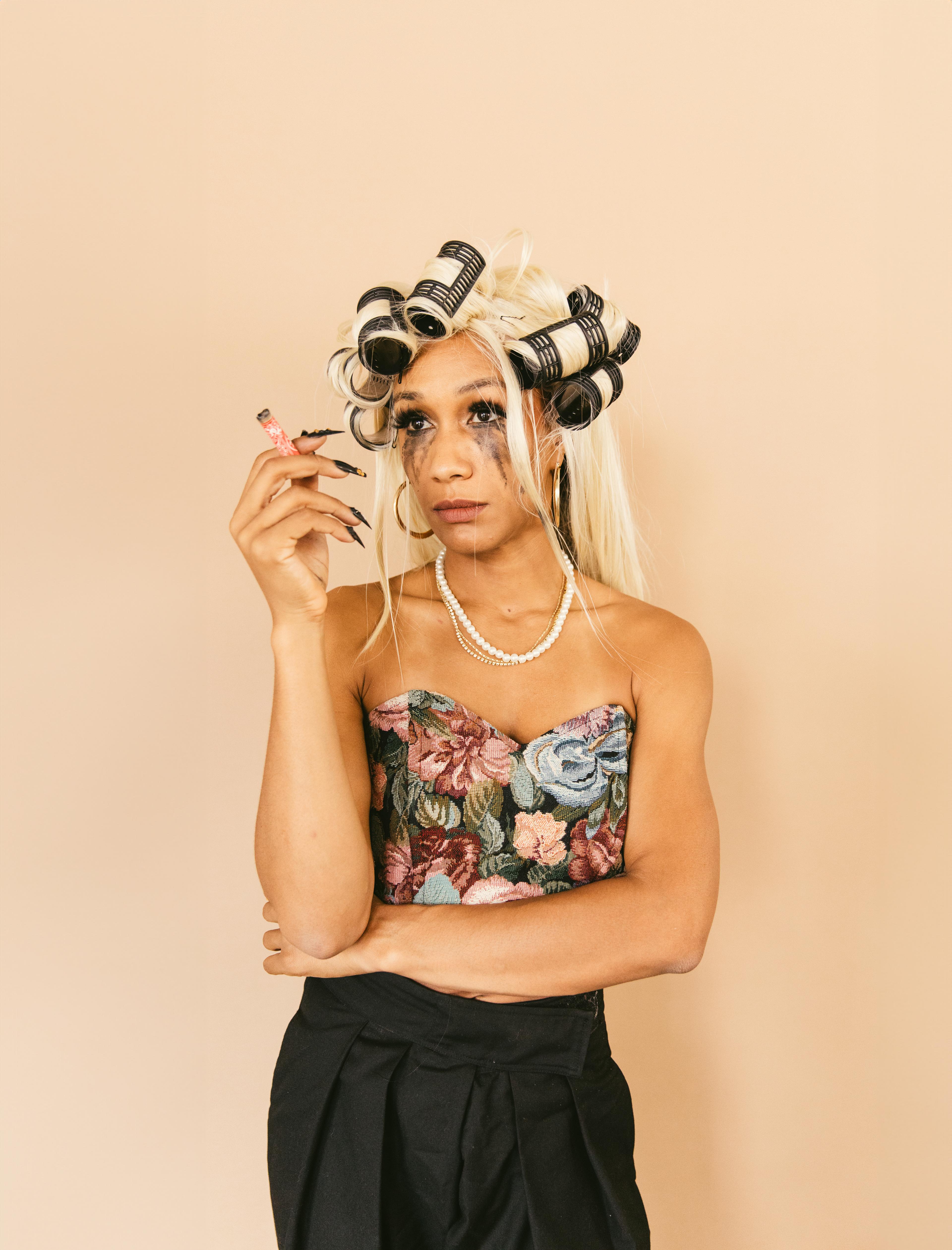 A person wearing curlers and with smudged mascara, holding a cigarette