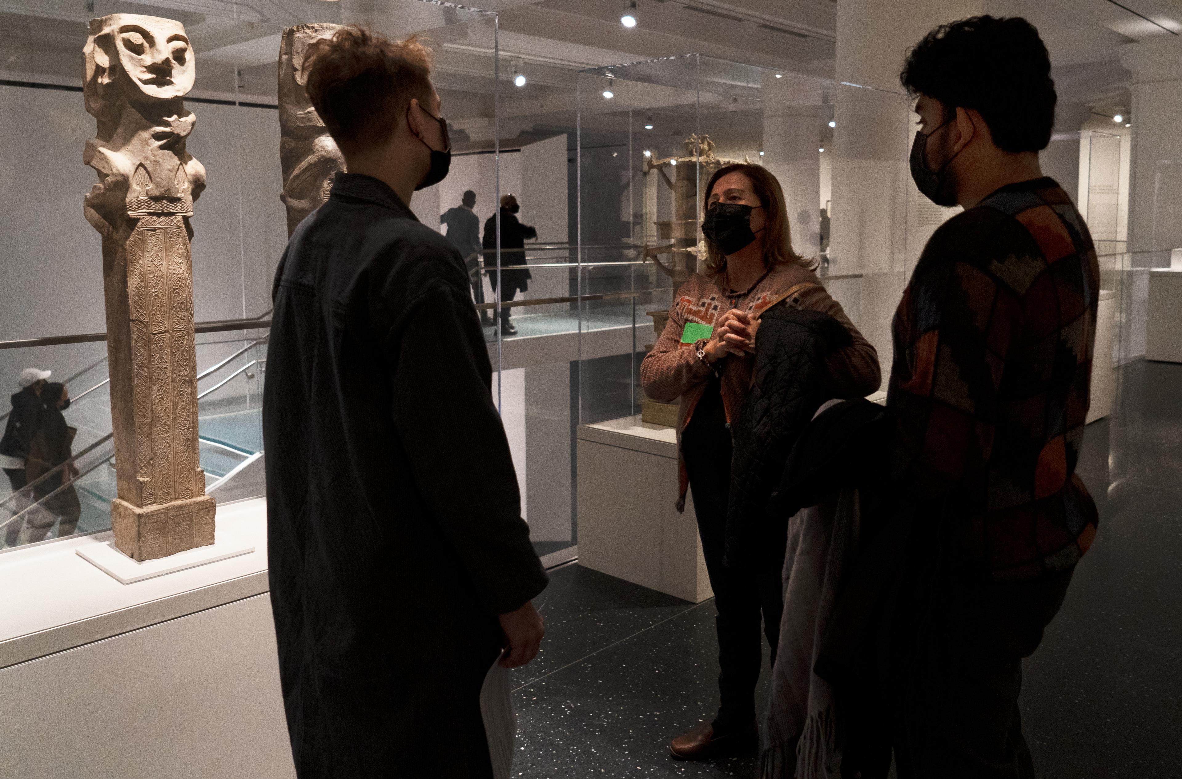 Three museum visitors speak to eachother near a sculpture