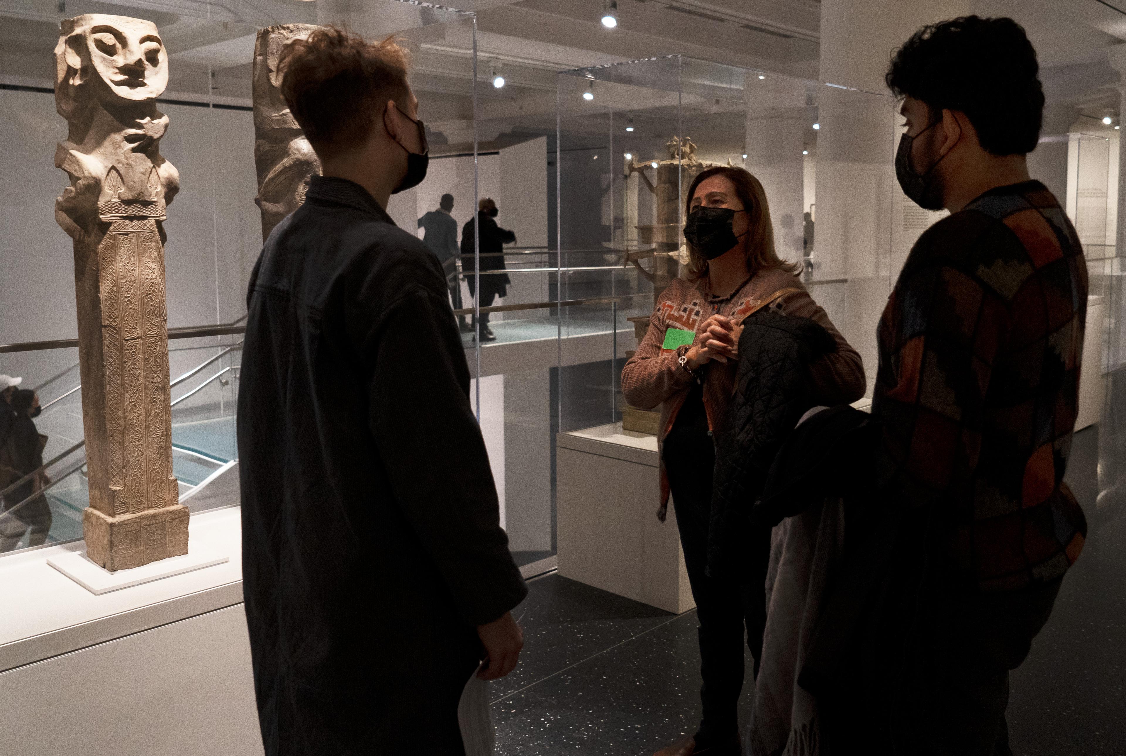 Three museum visitors speak to eachother near a sculpture