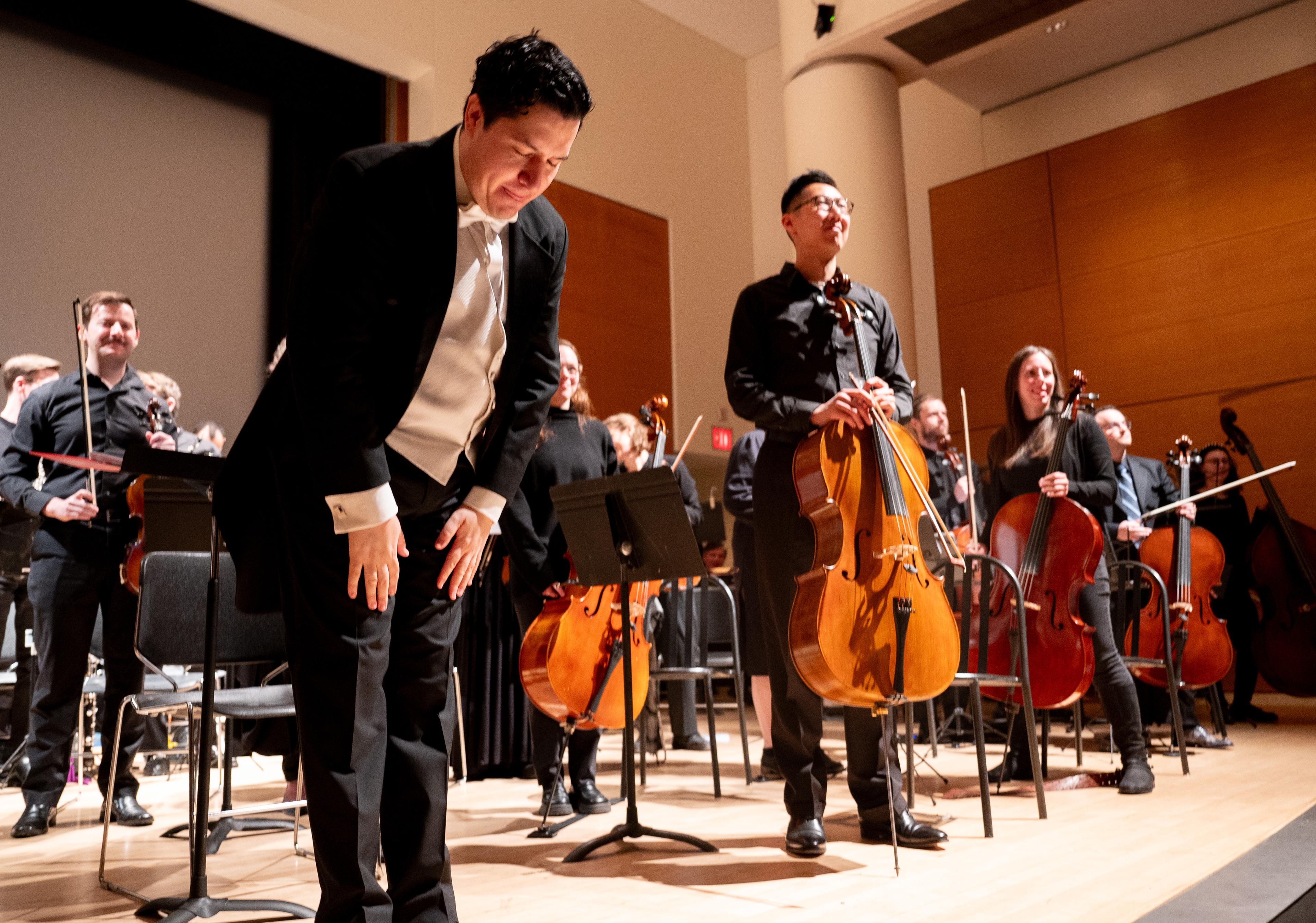 Orchestra and its conductor stands on stage bowing for the audience