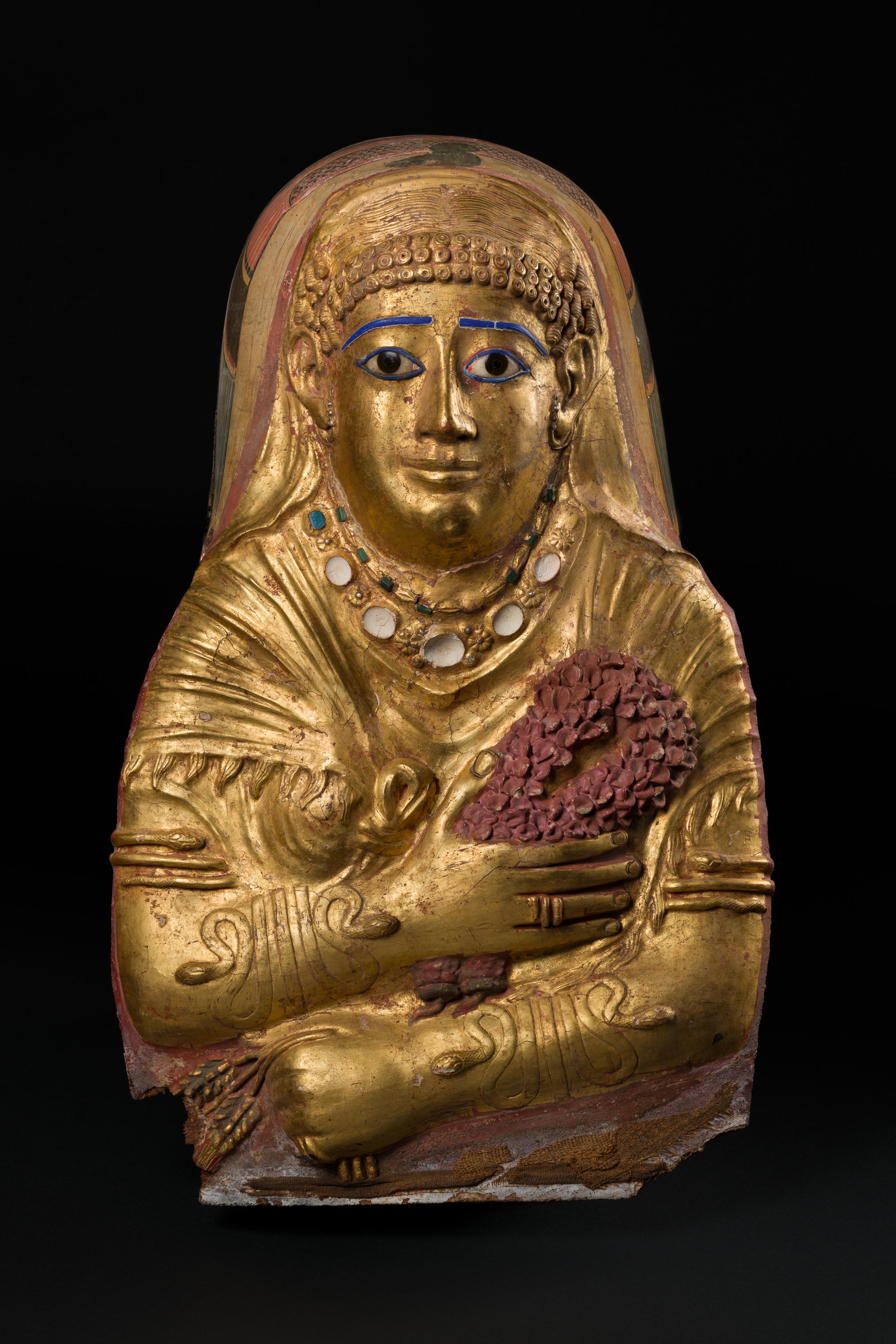 Gold mummy figure holding purple flowers set against a black backdrop